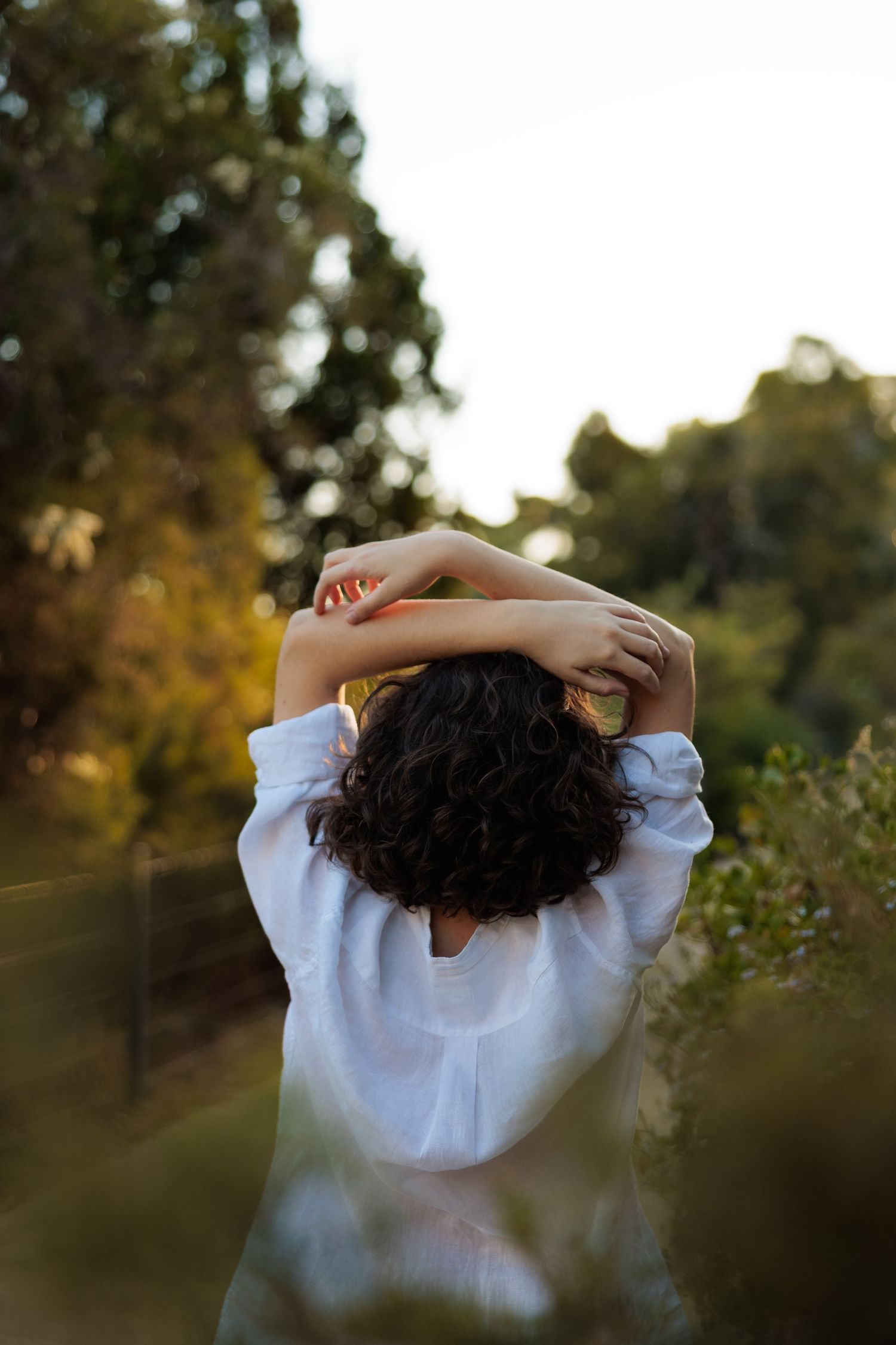 Back view of person in white shirt stretching arms in garden setting.