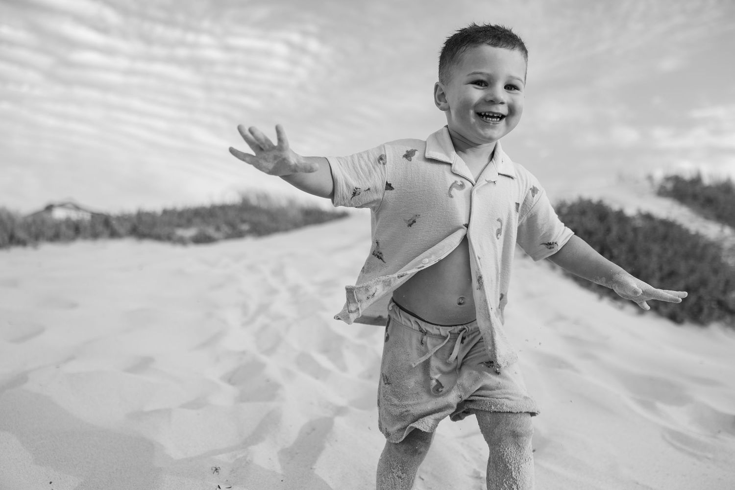 A series of black and white photos showing a toddler running and playing on a sandy beach.