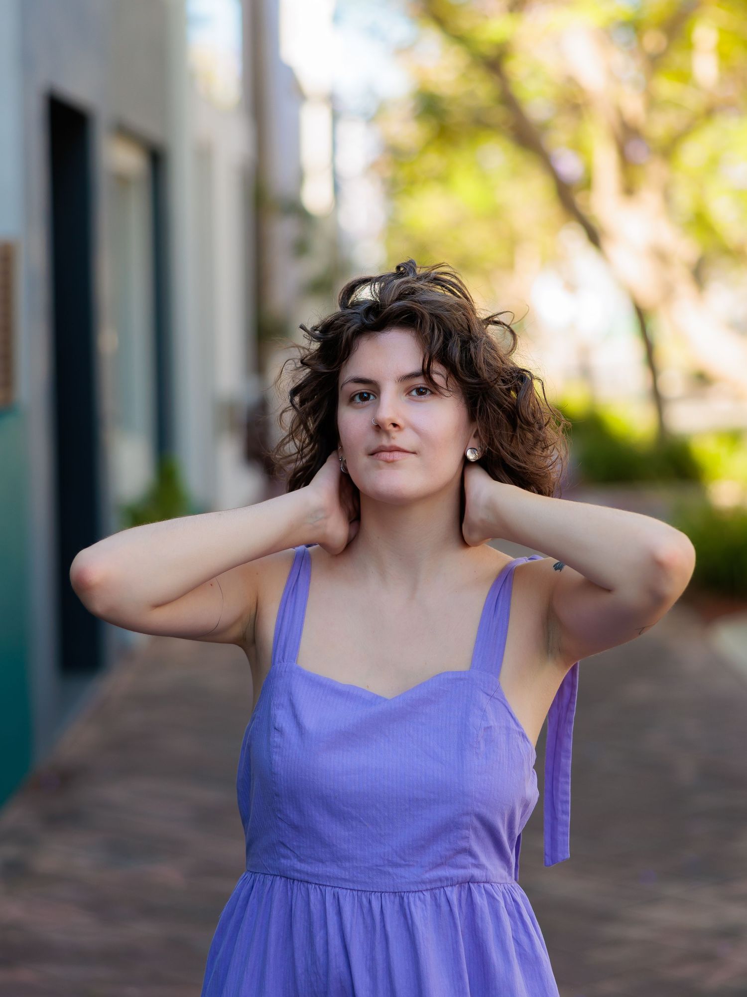 A person in a purple sundress poses playfully outdoors.
