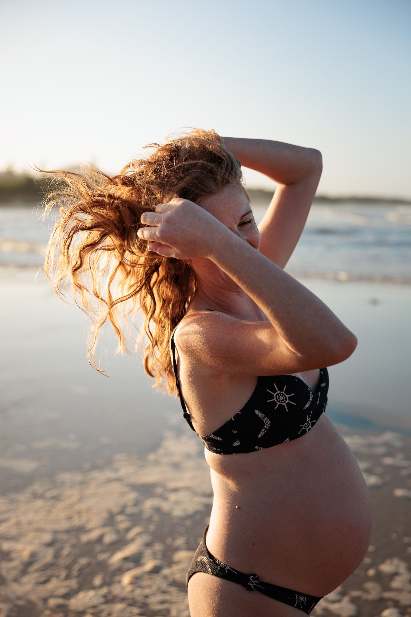 Maternity beach photoshoot with dramatic sunset lighting and ocean waves.
