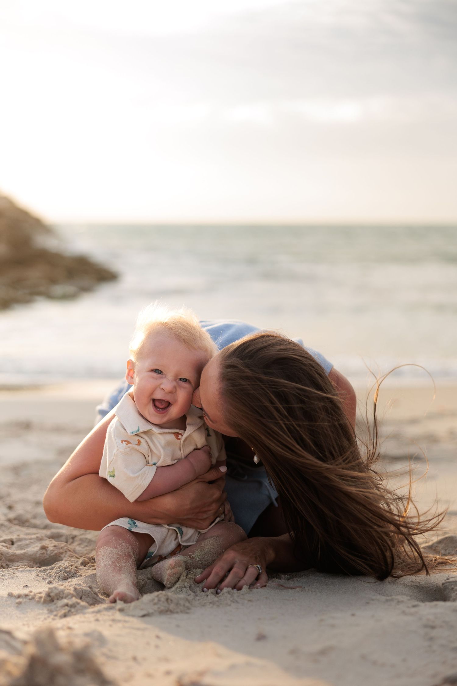 A tender beach moment captured in warm sunlight as parent and child play together in the sand.