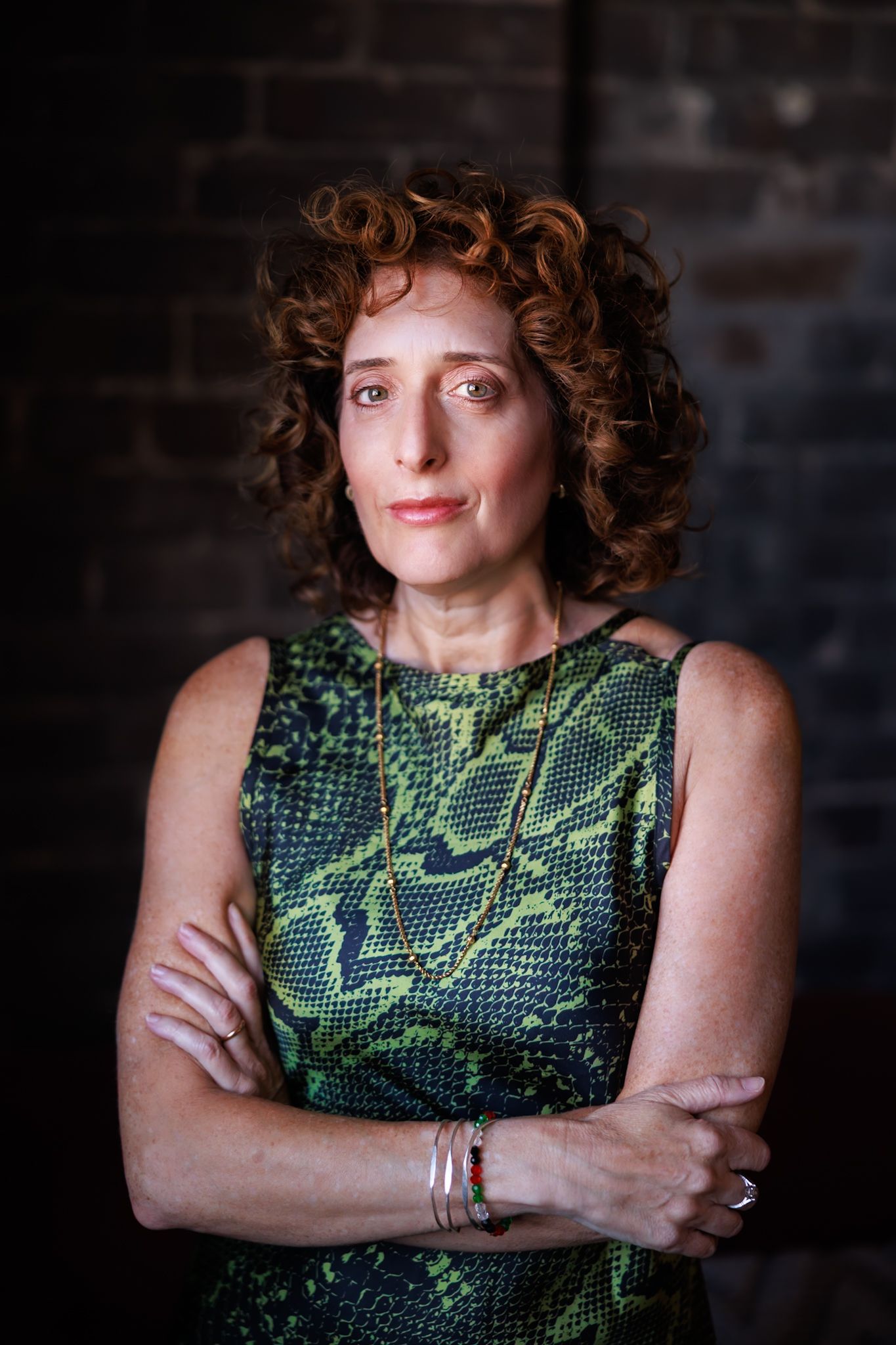 Portrait series in dark setting showing person in green patterned sleeveless top with curly hair against brick wall.