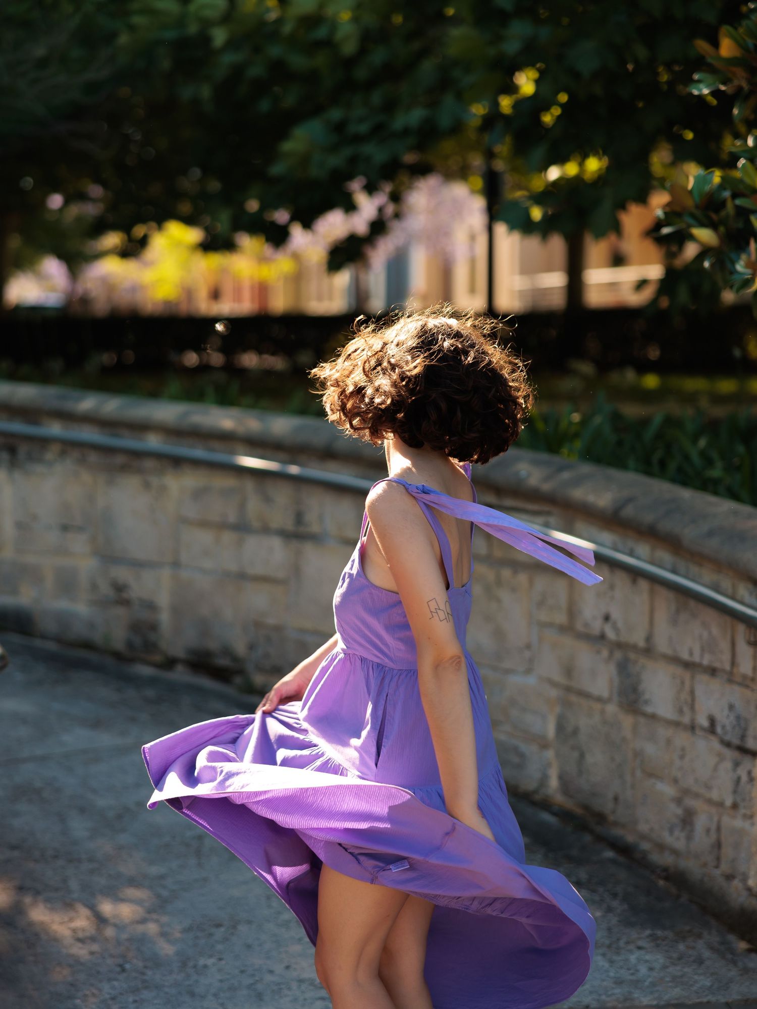 Flowing purple dress twirls gracefully in outdoor garden setting at sunset.