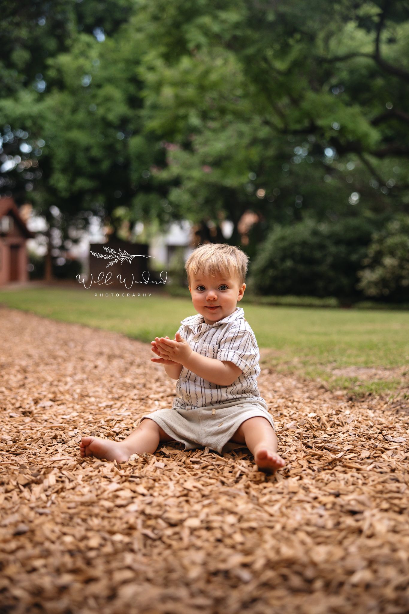 A small child sits and plays in a large pile of fallen autumn leaves in a park setting.