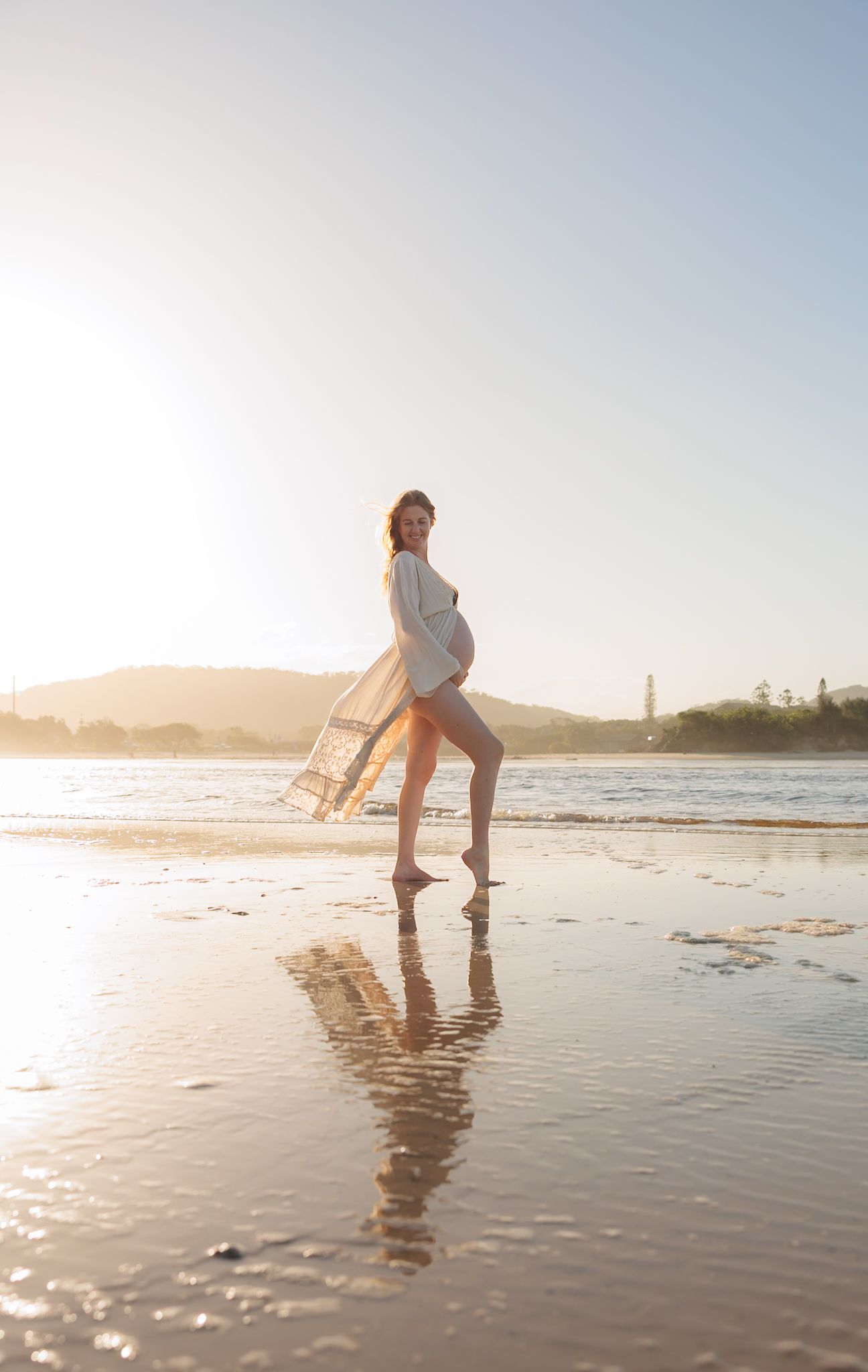 Child playing and splashing in shallow ocean water at sunset on a sandy beach with reflective wet sand.