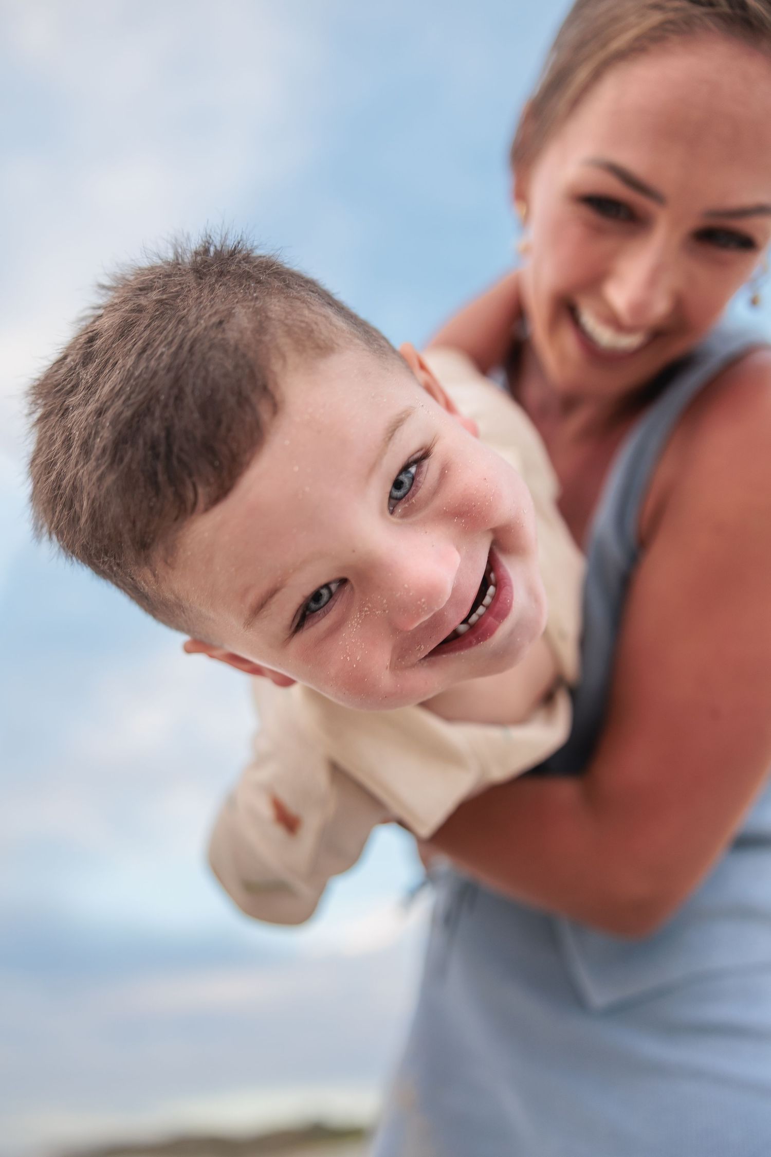 A playful moment captured outdoors as a child smiles while being held up against a blue sky background.