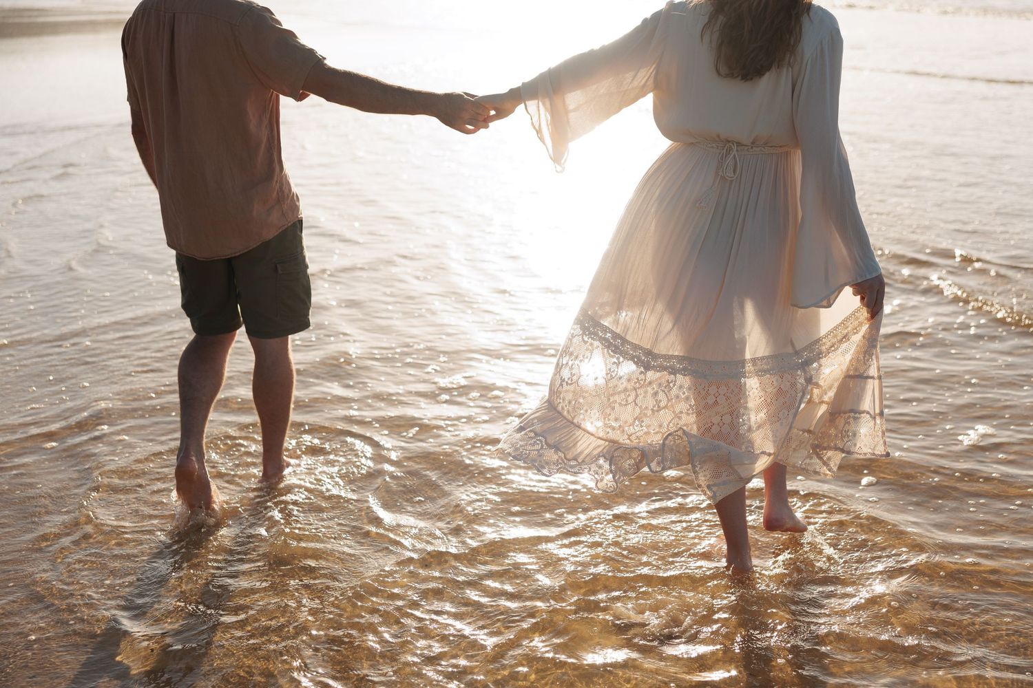 A couple walking together in shallow water during sunset.