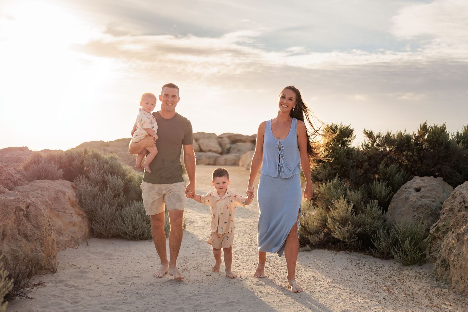 Family walking together along sandy path at sunset with mountains and desert landscape in background.