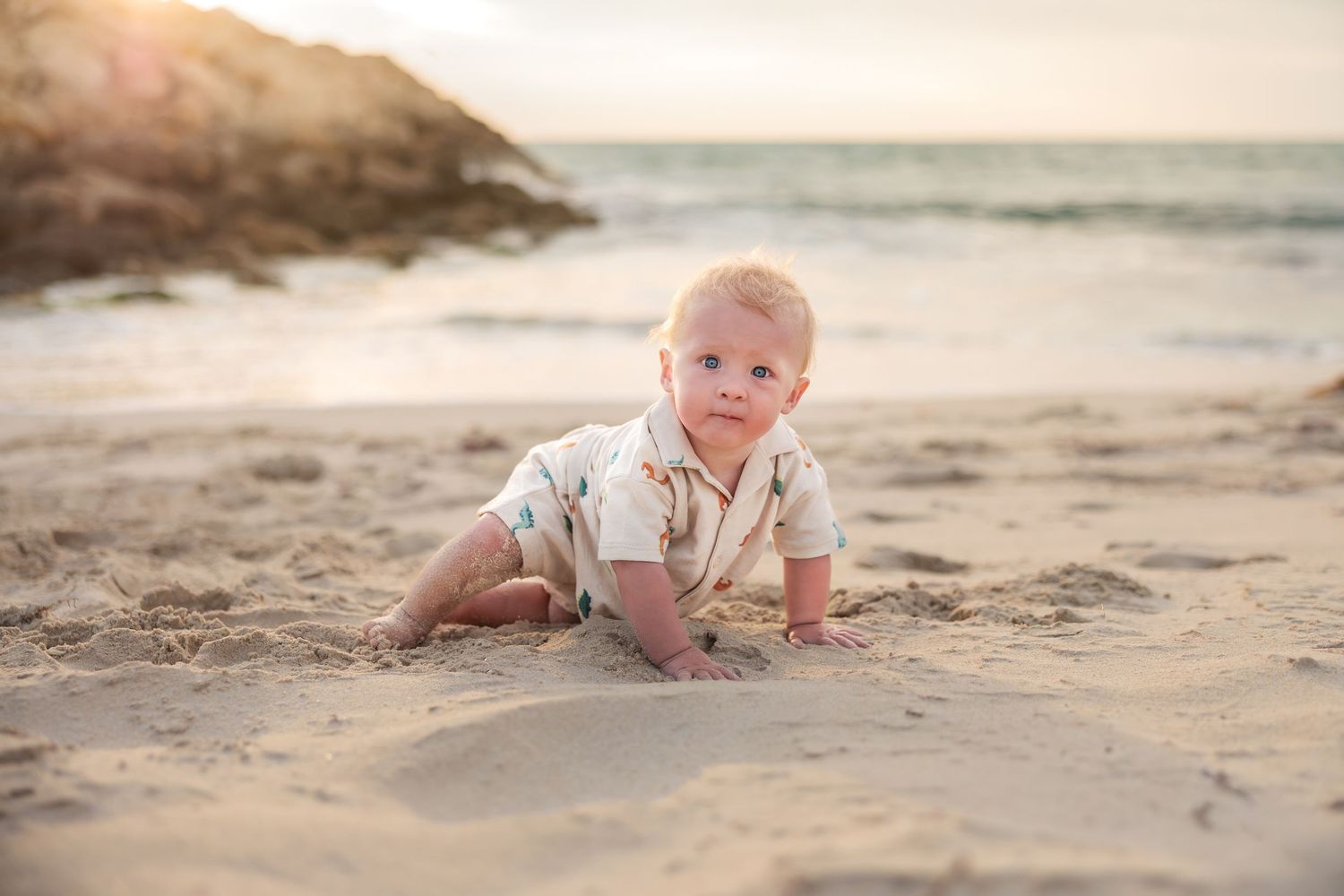 A series of photos showing a baby crawling and playing on a sandy beach at sunset with soft golden lighting.