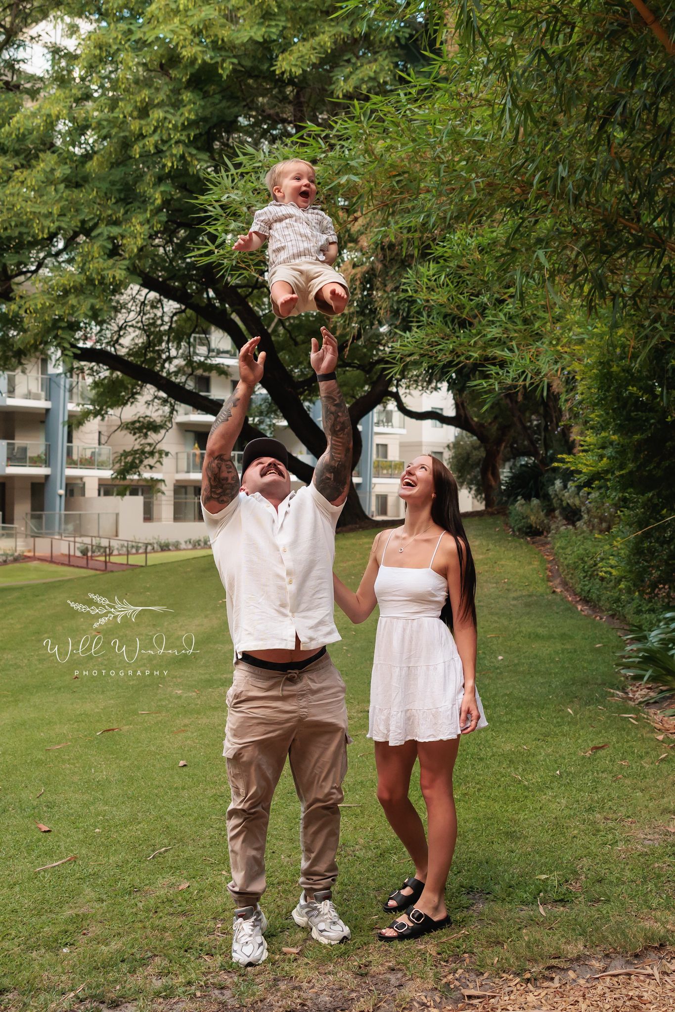 A couple dances and laughs together on a grassy lawn during a casual outdoor photoshoot.