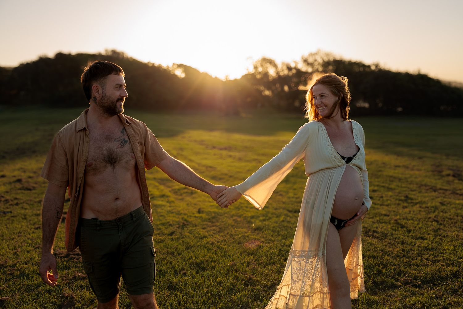 Couple walking through grassy field during sunset maternity session.