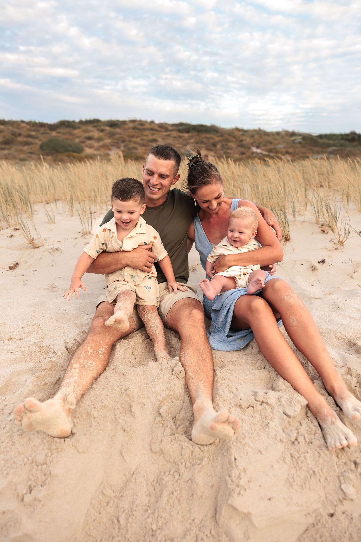 A family sits together on a sandy beach dune on a cloudy summer day.