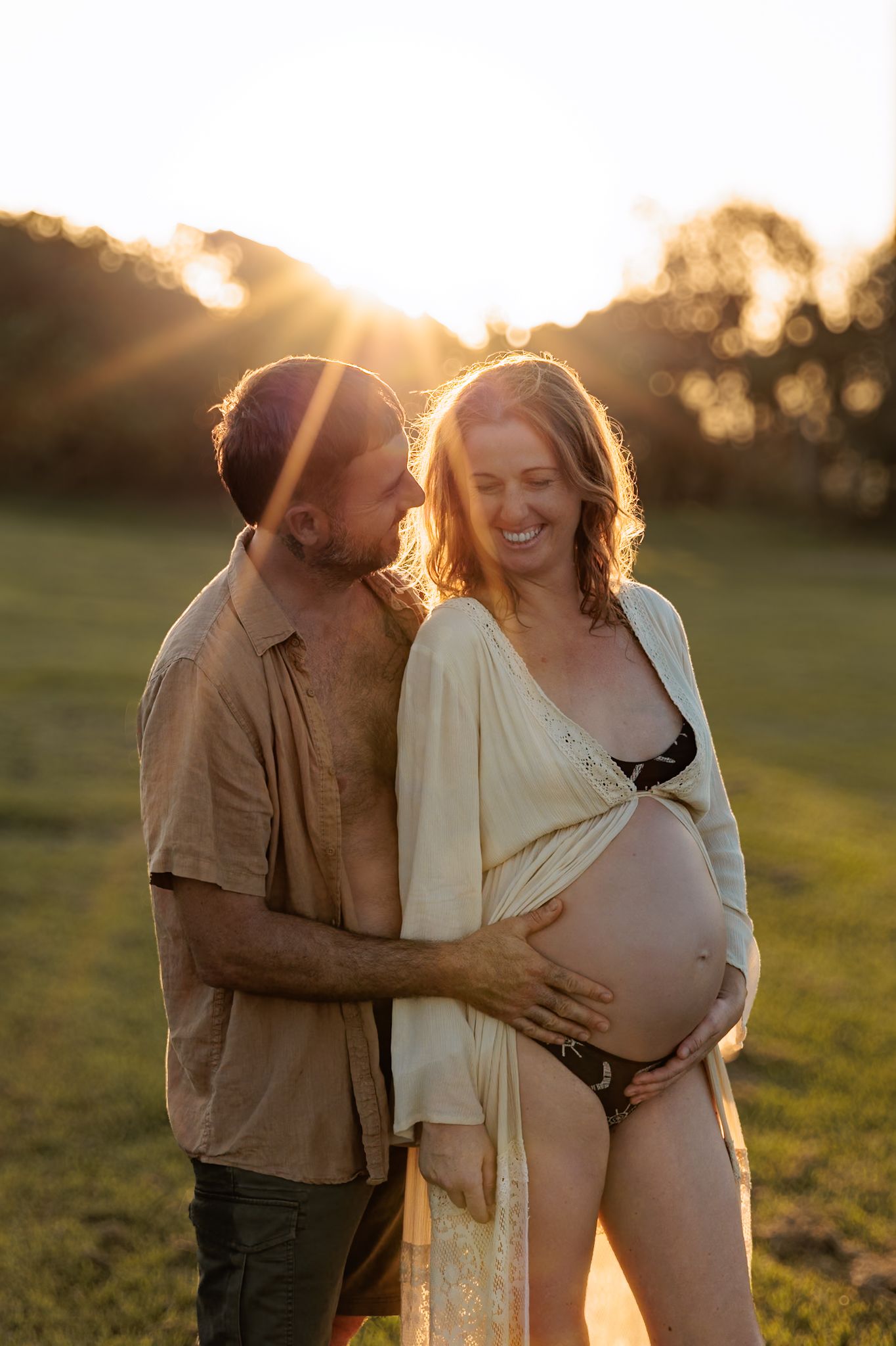 A couple shares intimate moments in a golden sunset field wearing neutral toned clothing.