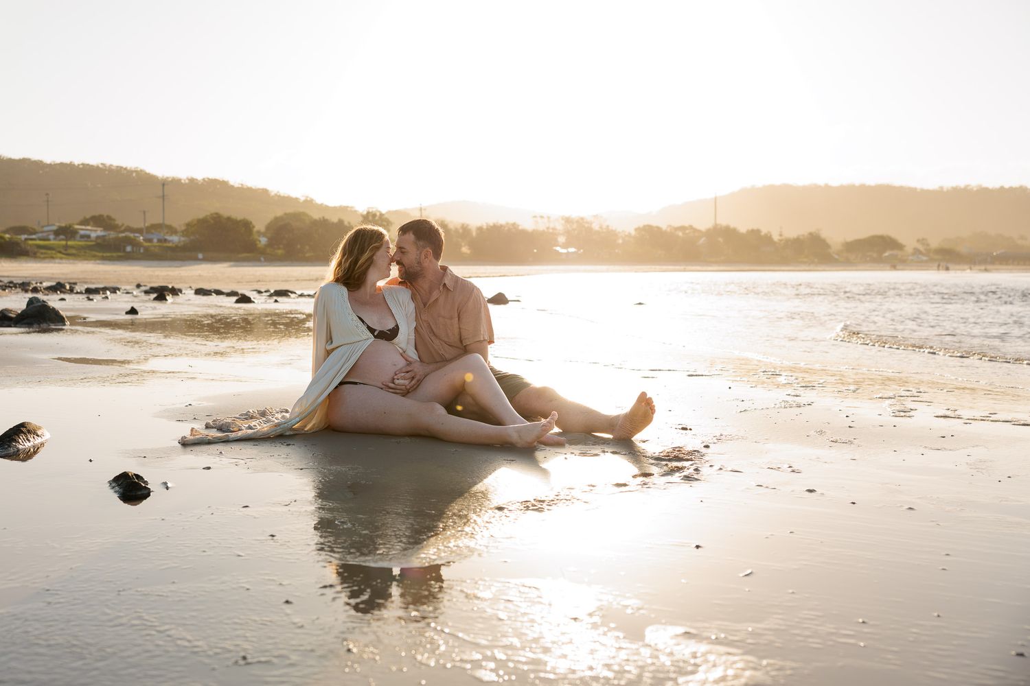Couple relaxing on sandy beach during golden hour photoshoot.
