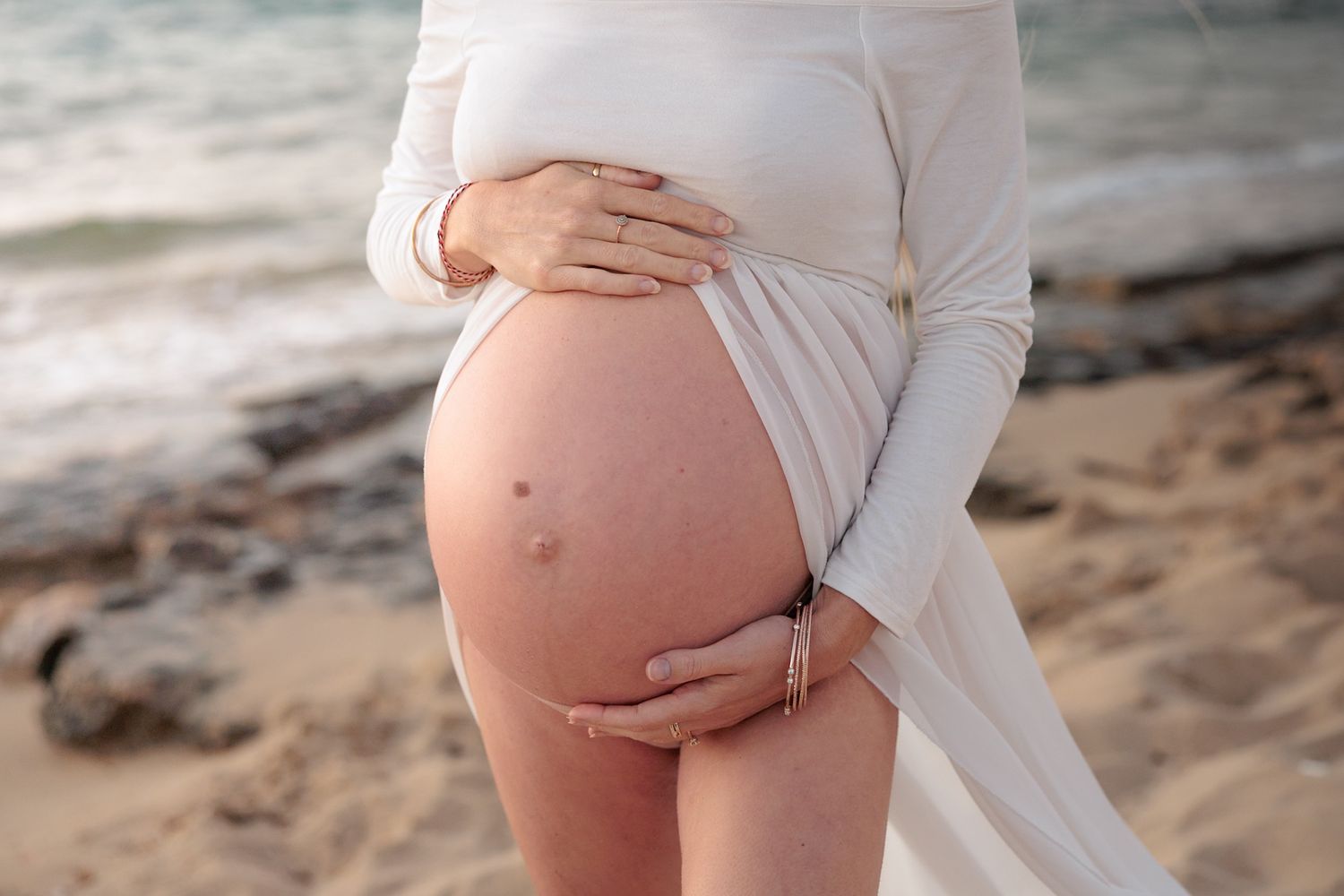 A series of maternity photos showing a pregnant belly at sunset on a sandy beach in white clothing.