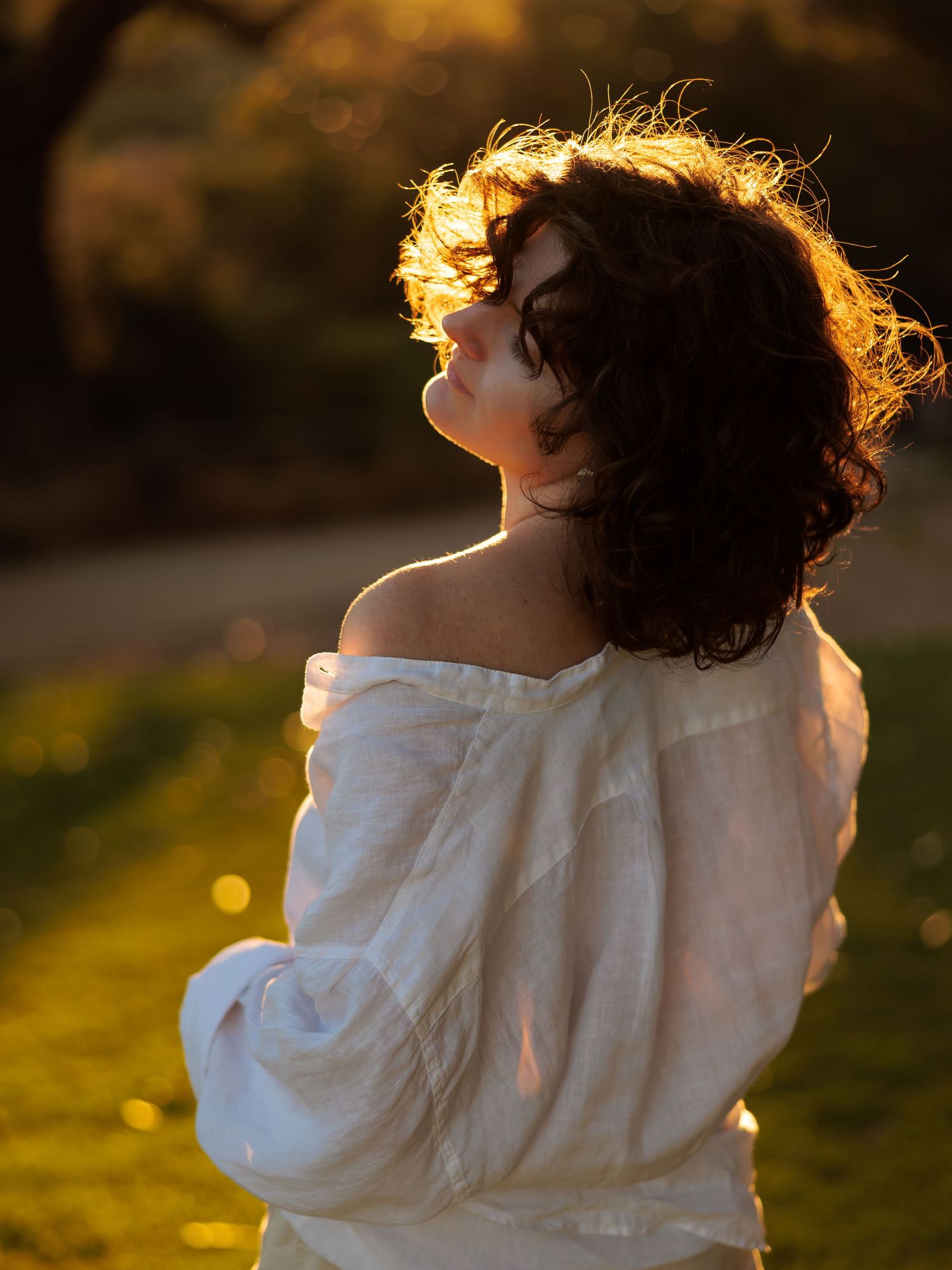 Person in white shirt illuminated by golden sunset light in garden setting.