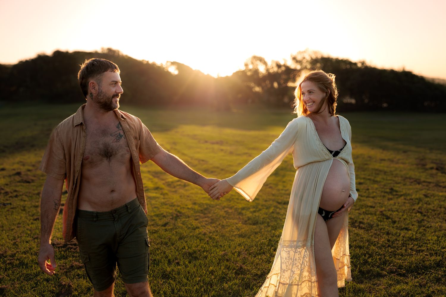 Romantic couple in a sunlit meadow at golden hour with flowing white dress and rustic attire.