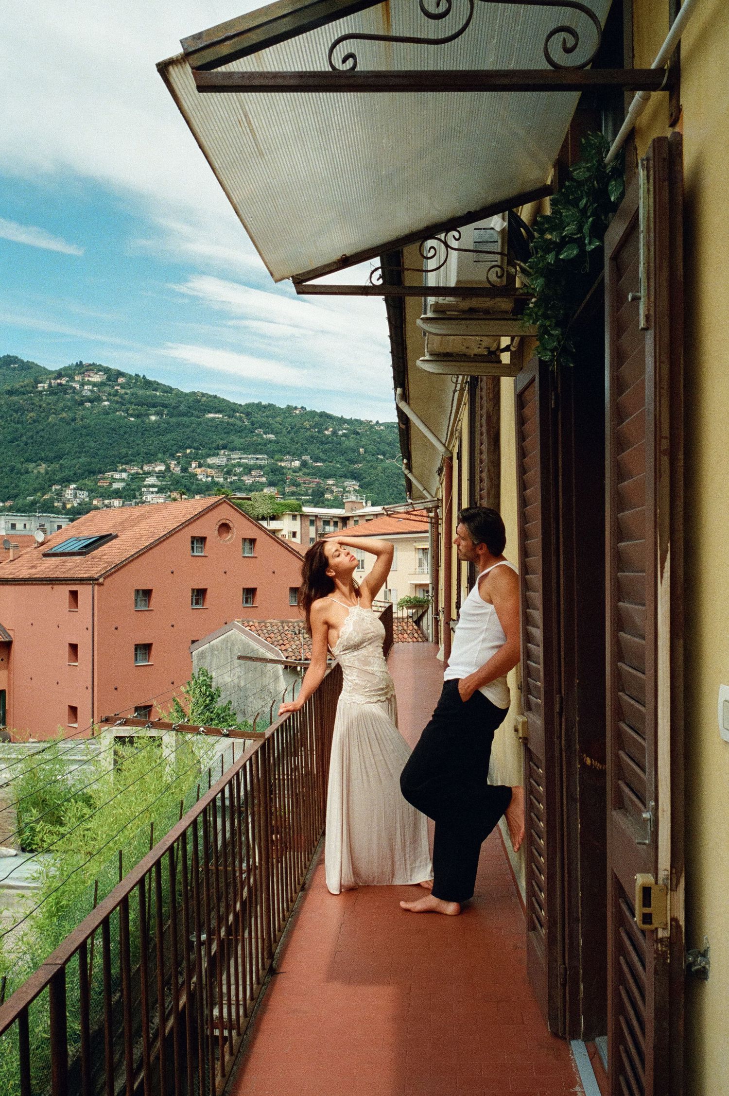 Elegant couple posing on a scenic Italian balcony with terracotta rooftops and green hills.