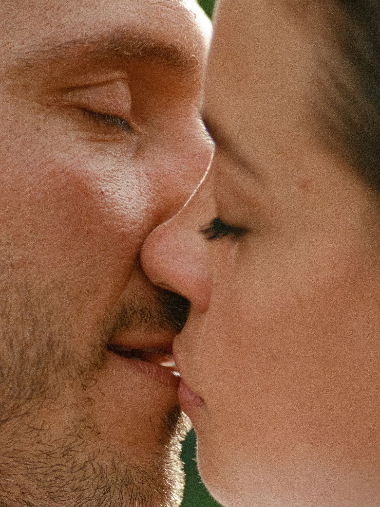 Close-up side profile of a couple sharing a romantic kiss in bright natural sunlight.