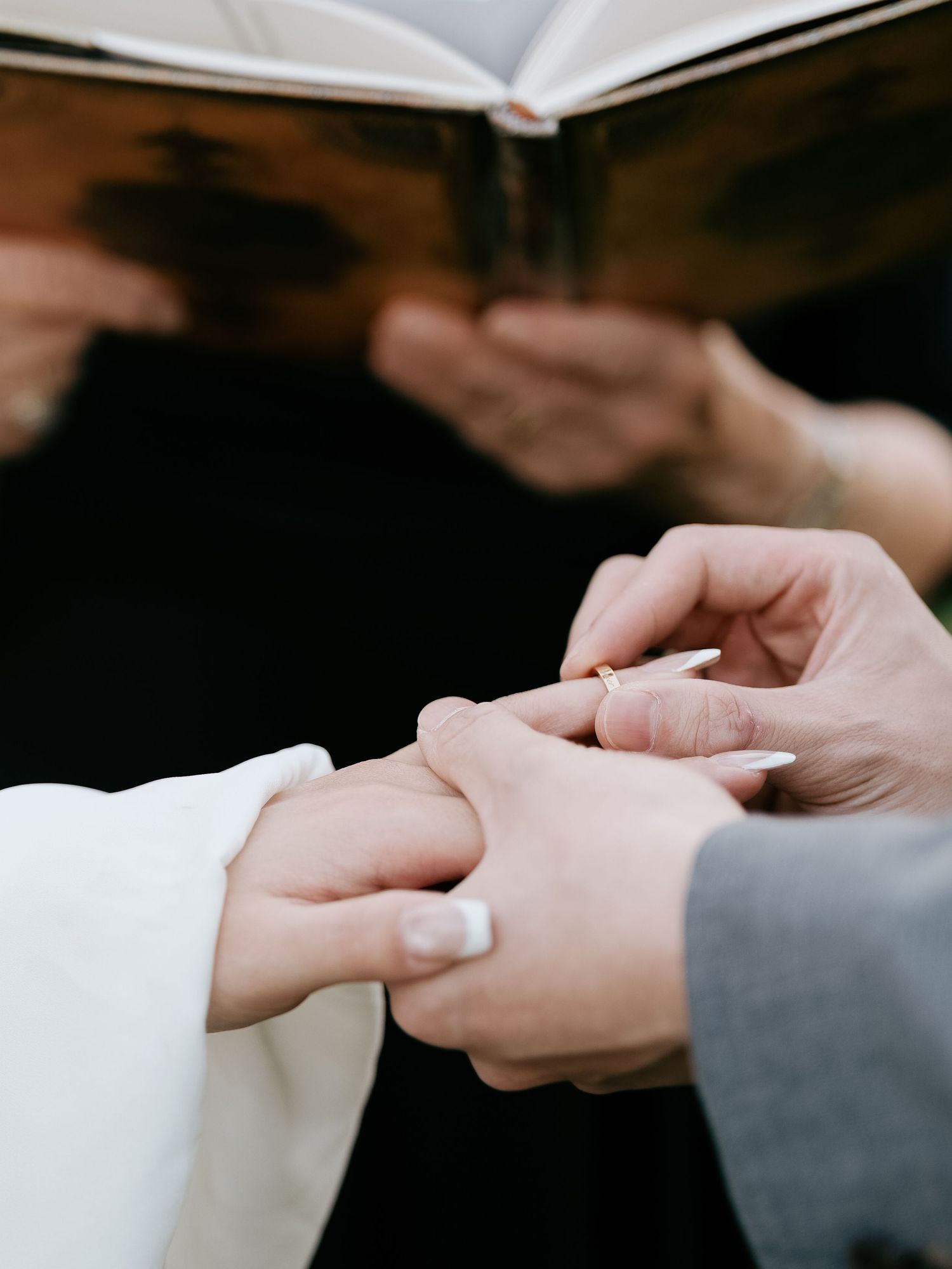 Close-up of groom placing gold wedding ring on bride's finger during ceremony.