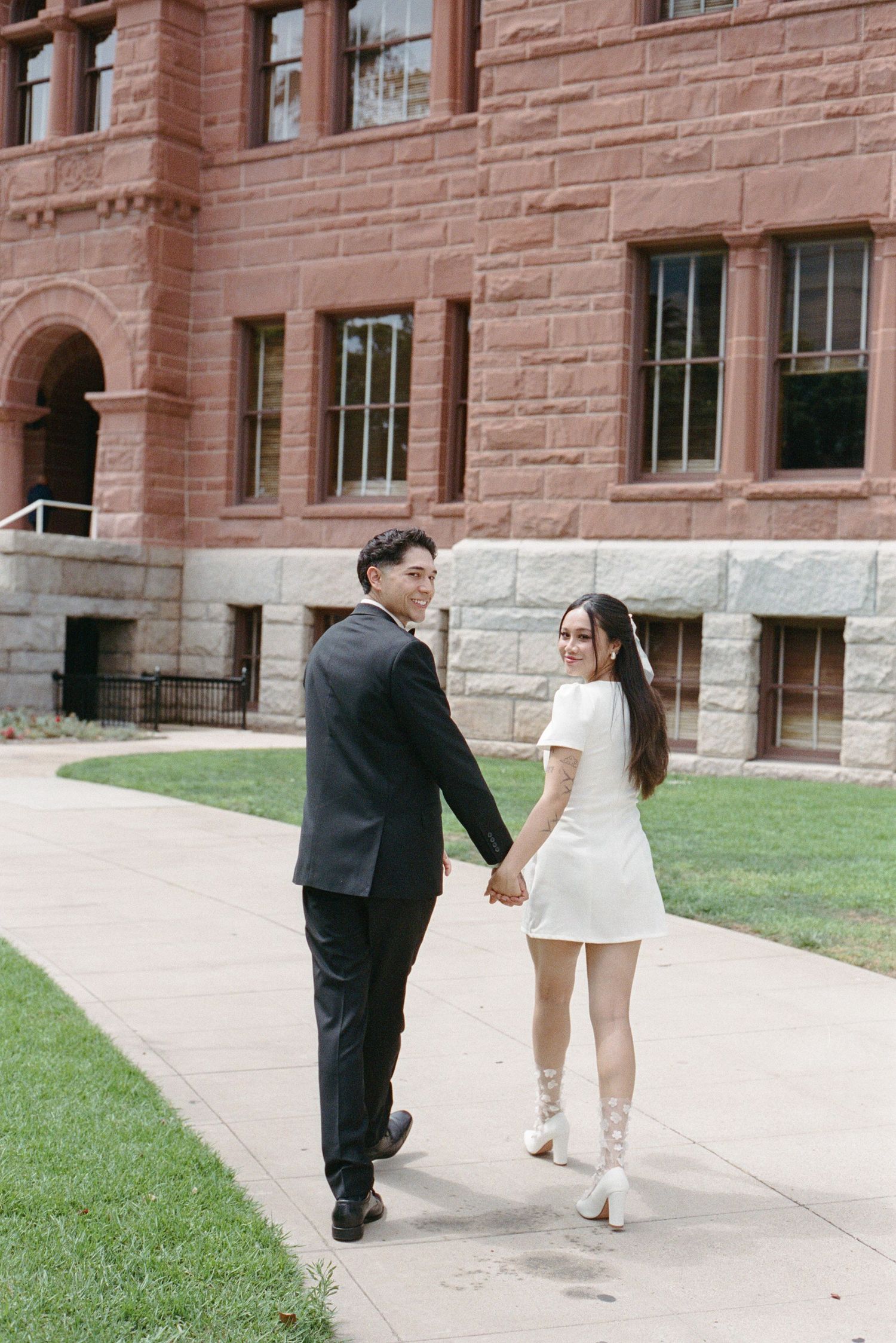 Newlywed couple holding hands walking away from historic red brick building after courthouse wedding.