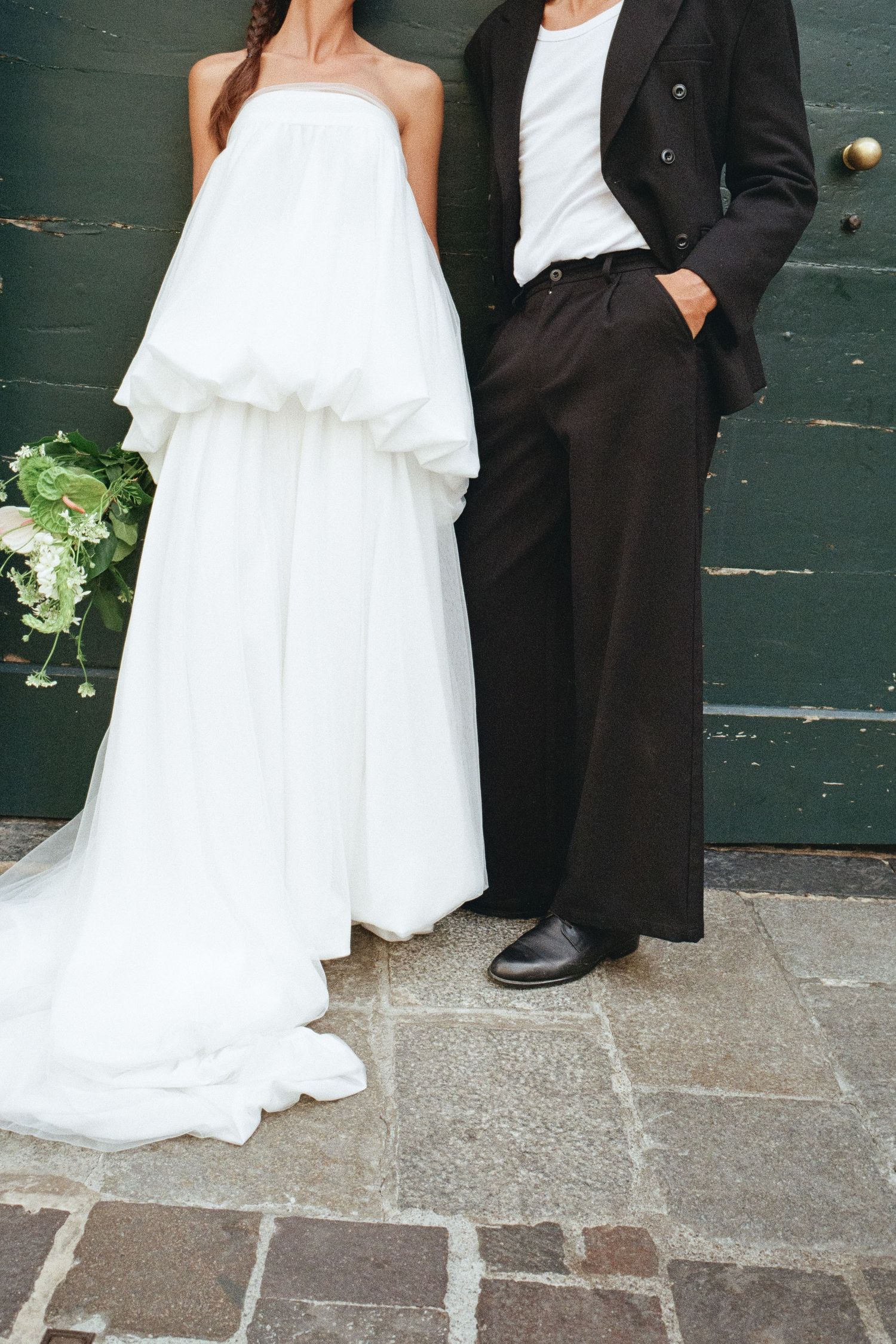 Close-up of bride in layered white strapless gown and groom in black suit by green door.