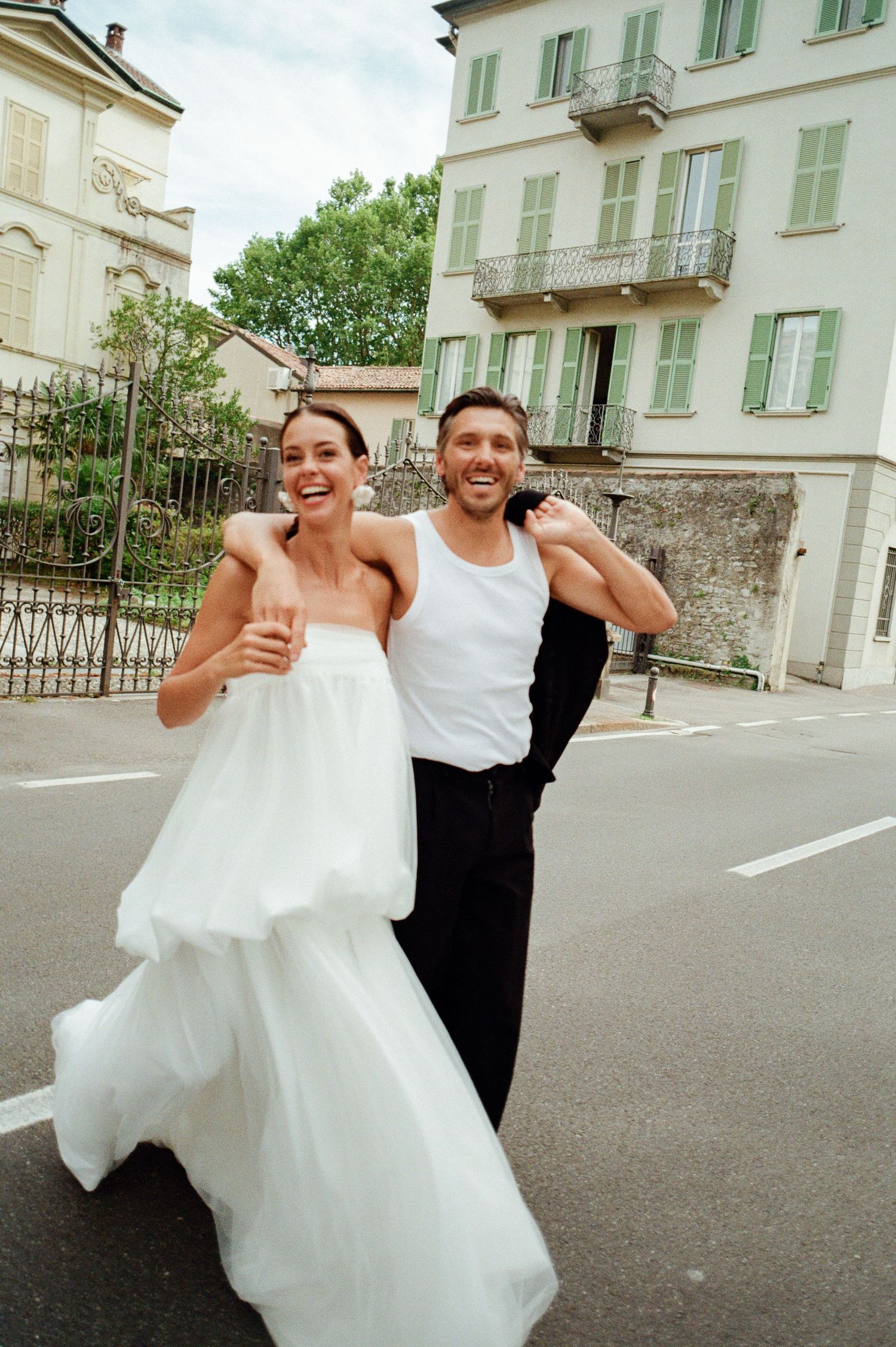 Happy bride and groom laughing while walking together on a sunny European street.