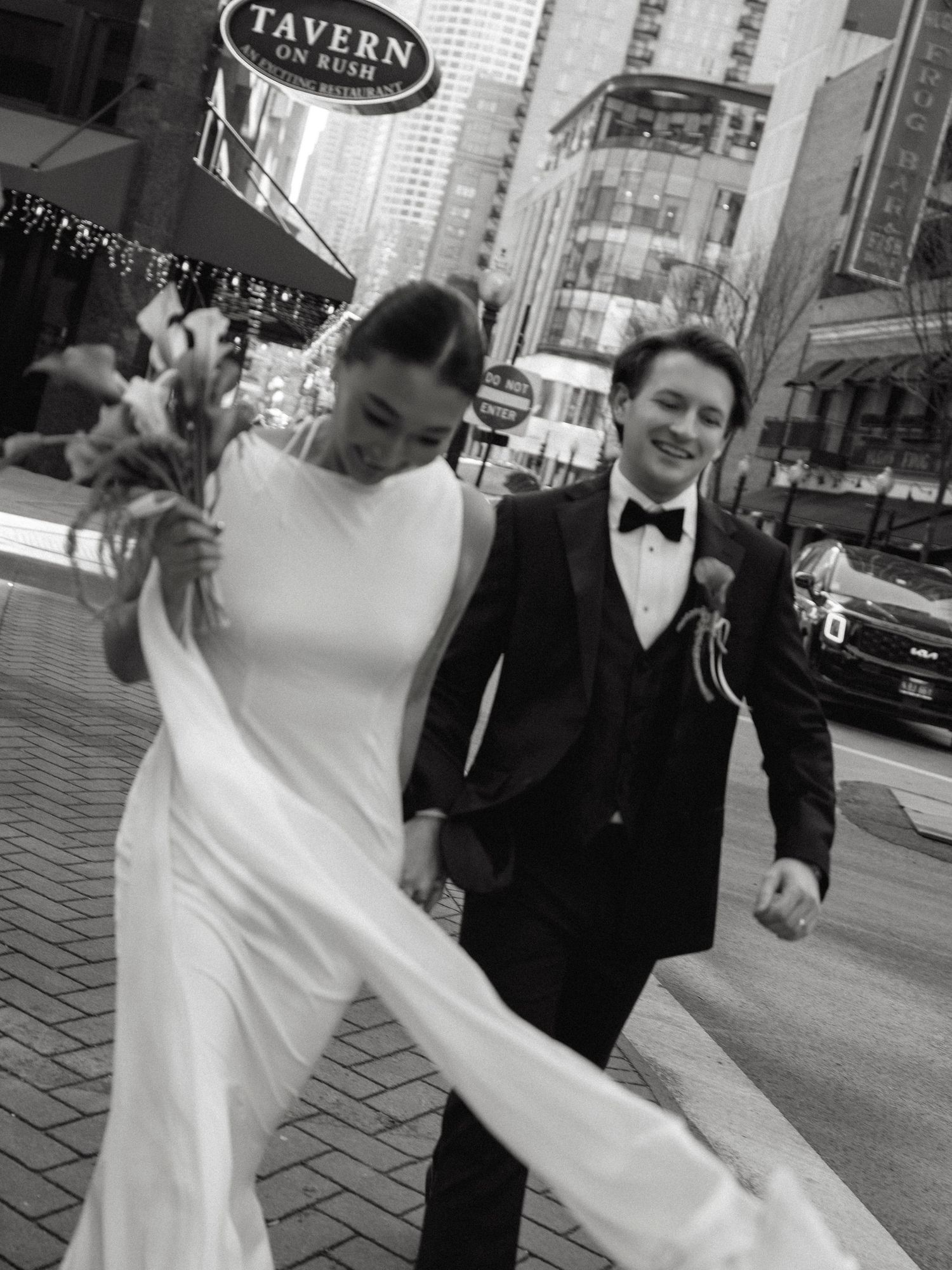 Black and white photo of smiling couple walking hand in hand past Tavern on Rush in Chicago.