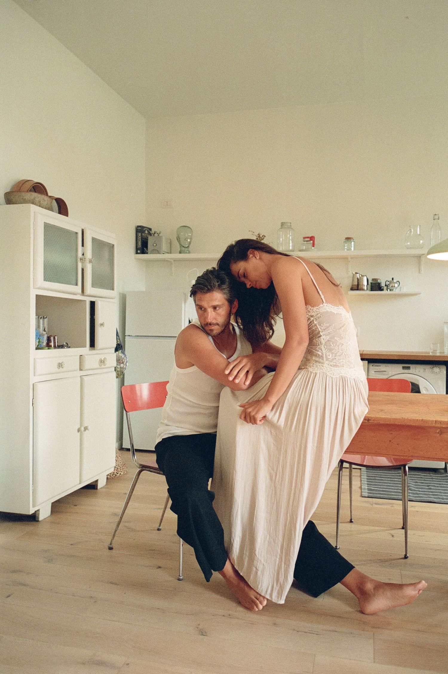 Couple in white outfits sharing a tender dance moment in a bright modern kitchen.