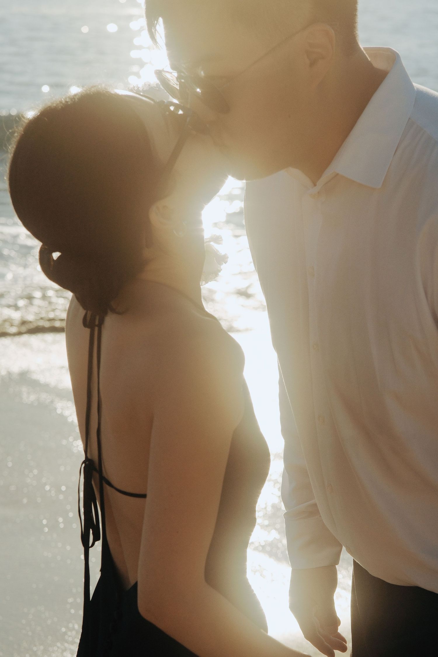 Couple sharing romantic kiss backlit by golden sunset light on beach.