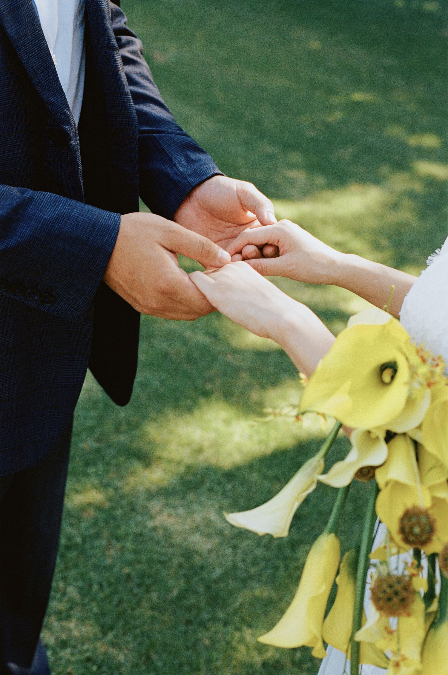 Groom places wedding ring on bride's finger as she holds a yellow calla lily bouquet.