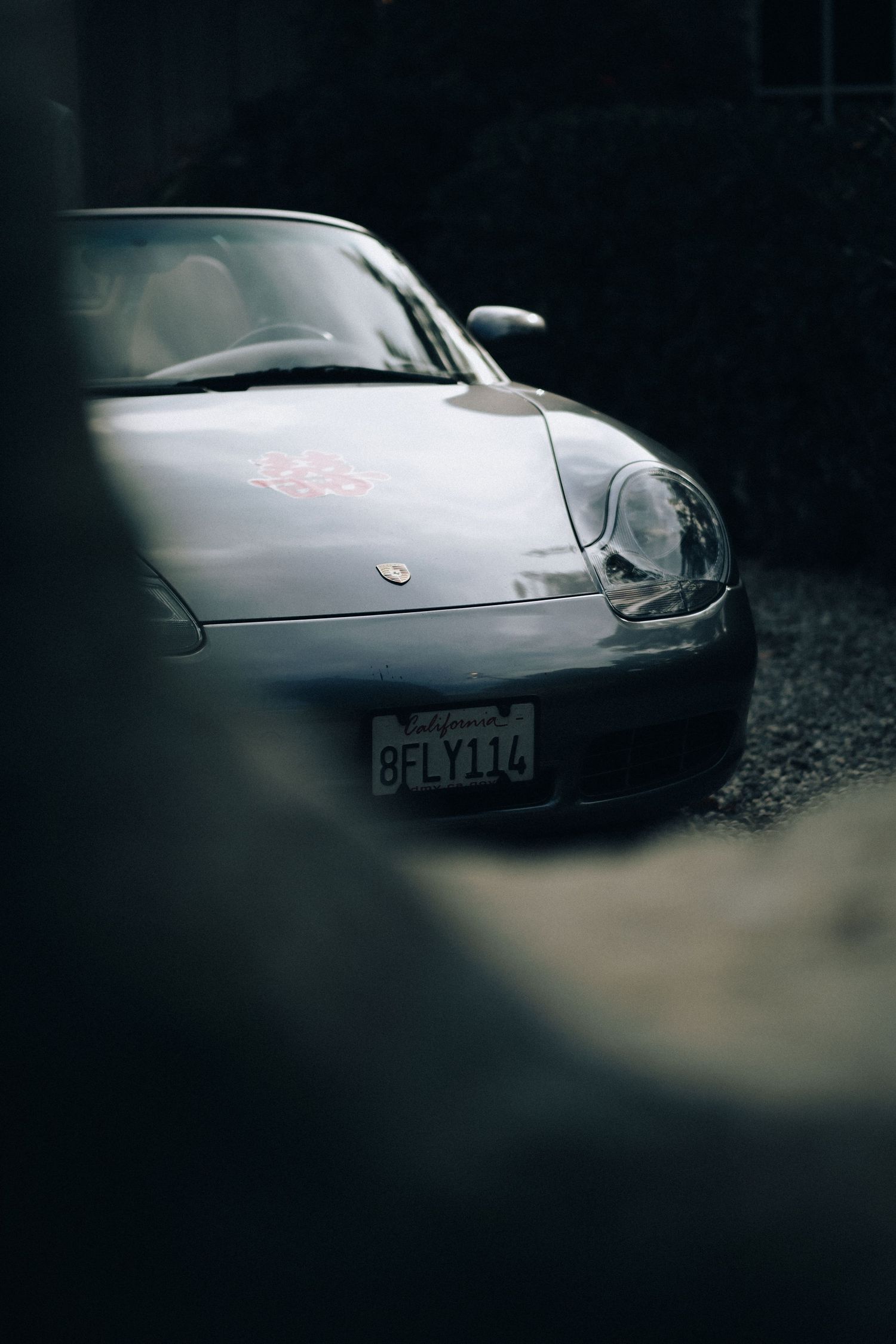 Silver Porsche 911 with a California license plate parked on a gravel driveway in moody low-light setting.