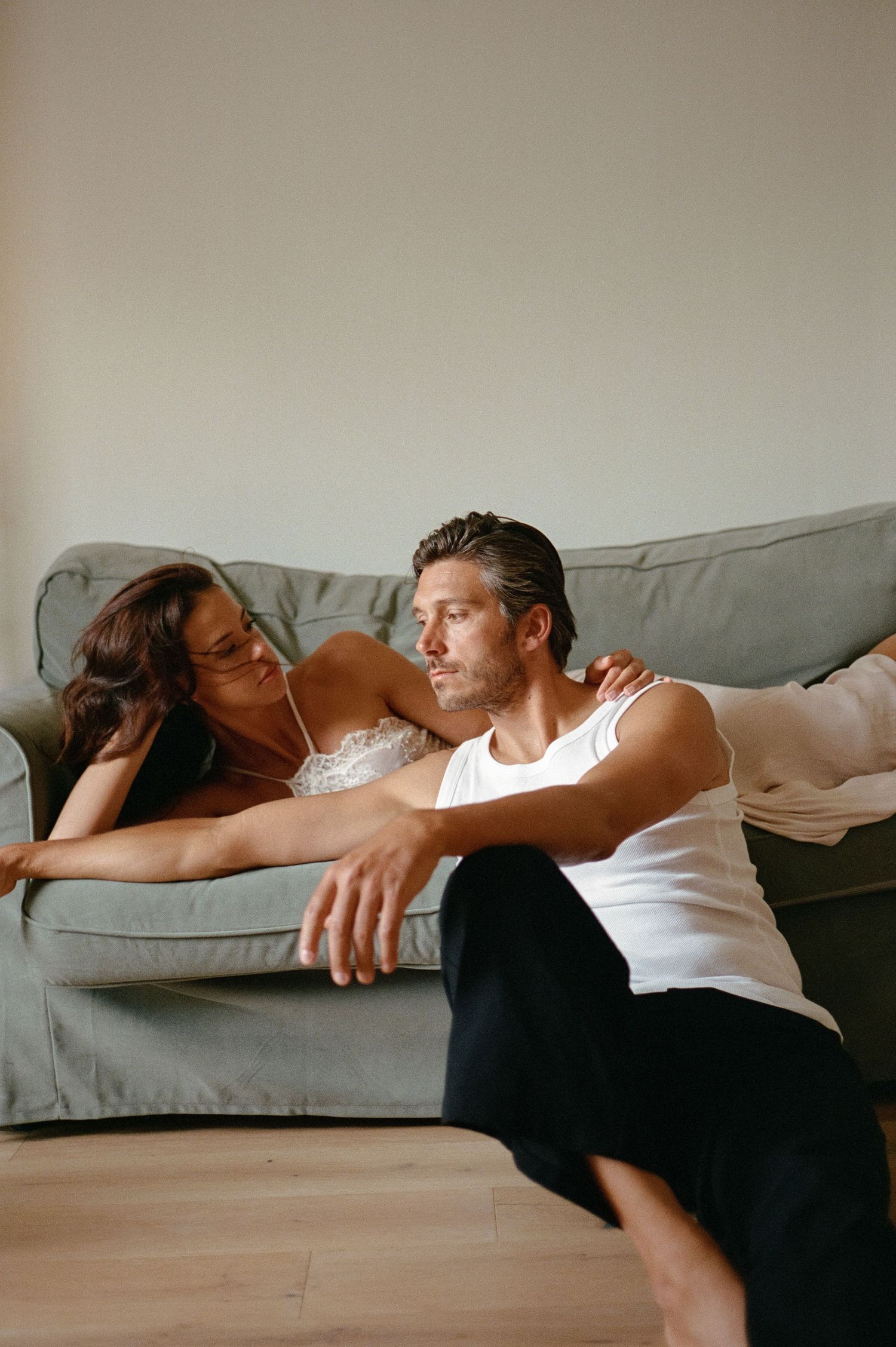 Couple sharing a quiet intimate moment together on a grey sofa in a softly lit room.