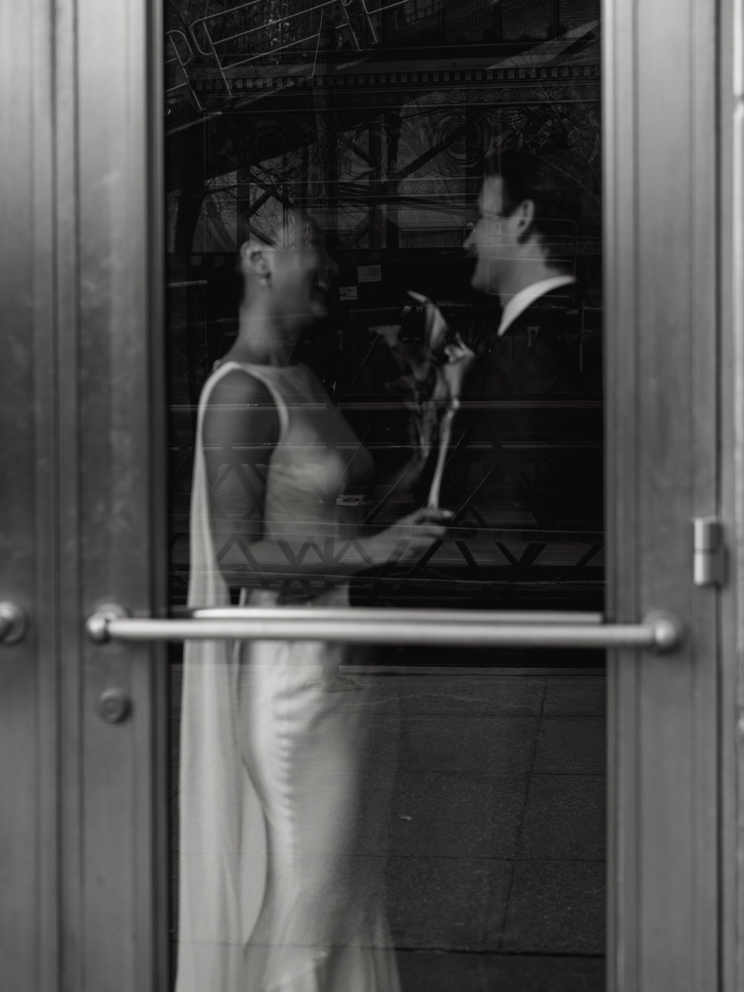 Black and white reflection of bride and groom sharing an intimate moment through glass door.