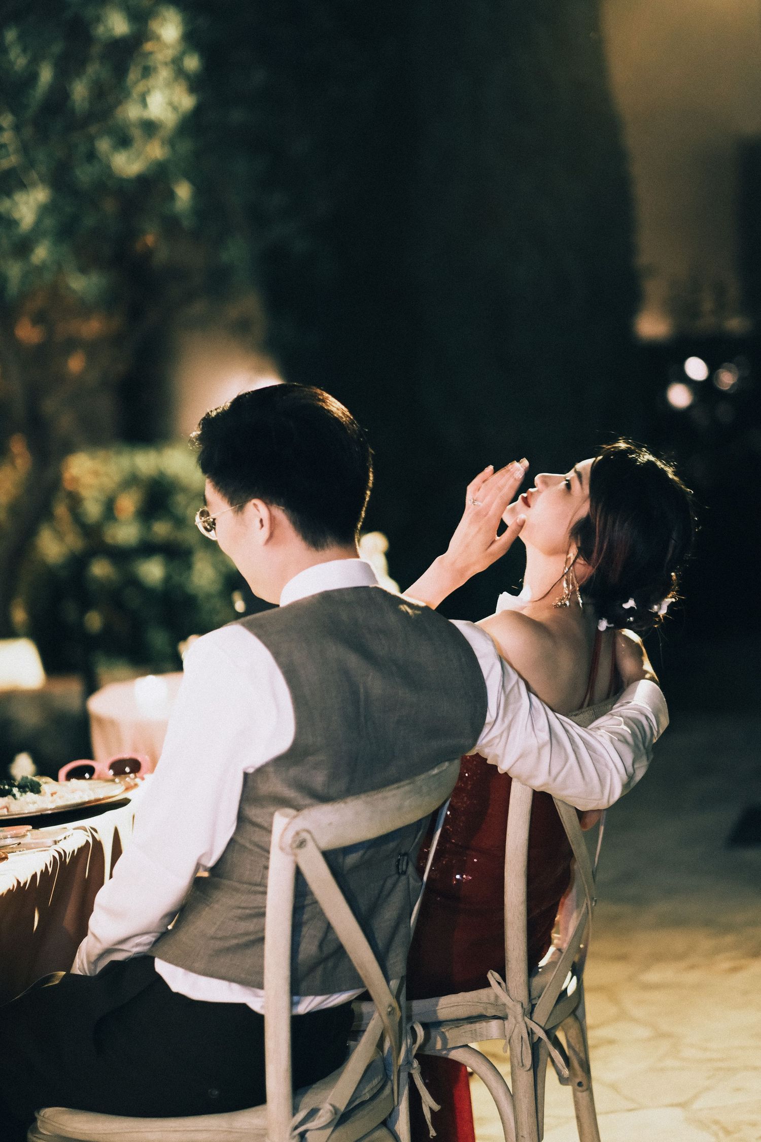 Couple shares intimate moment at wedding reception dinner table at night.