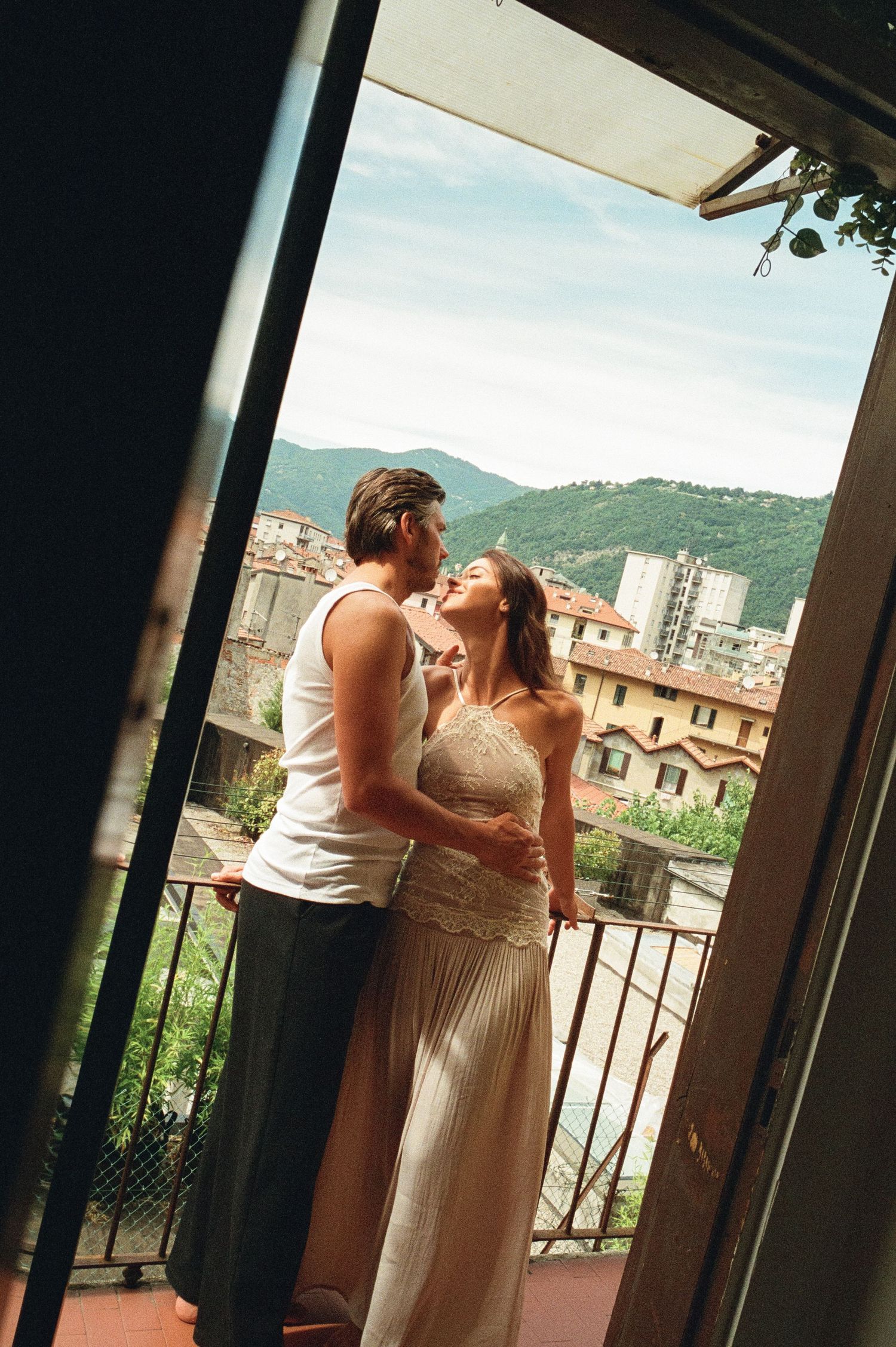 Couple sharing a romantic kiss on a balcony overlooking a picturesque Italian hillside city.