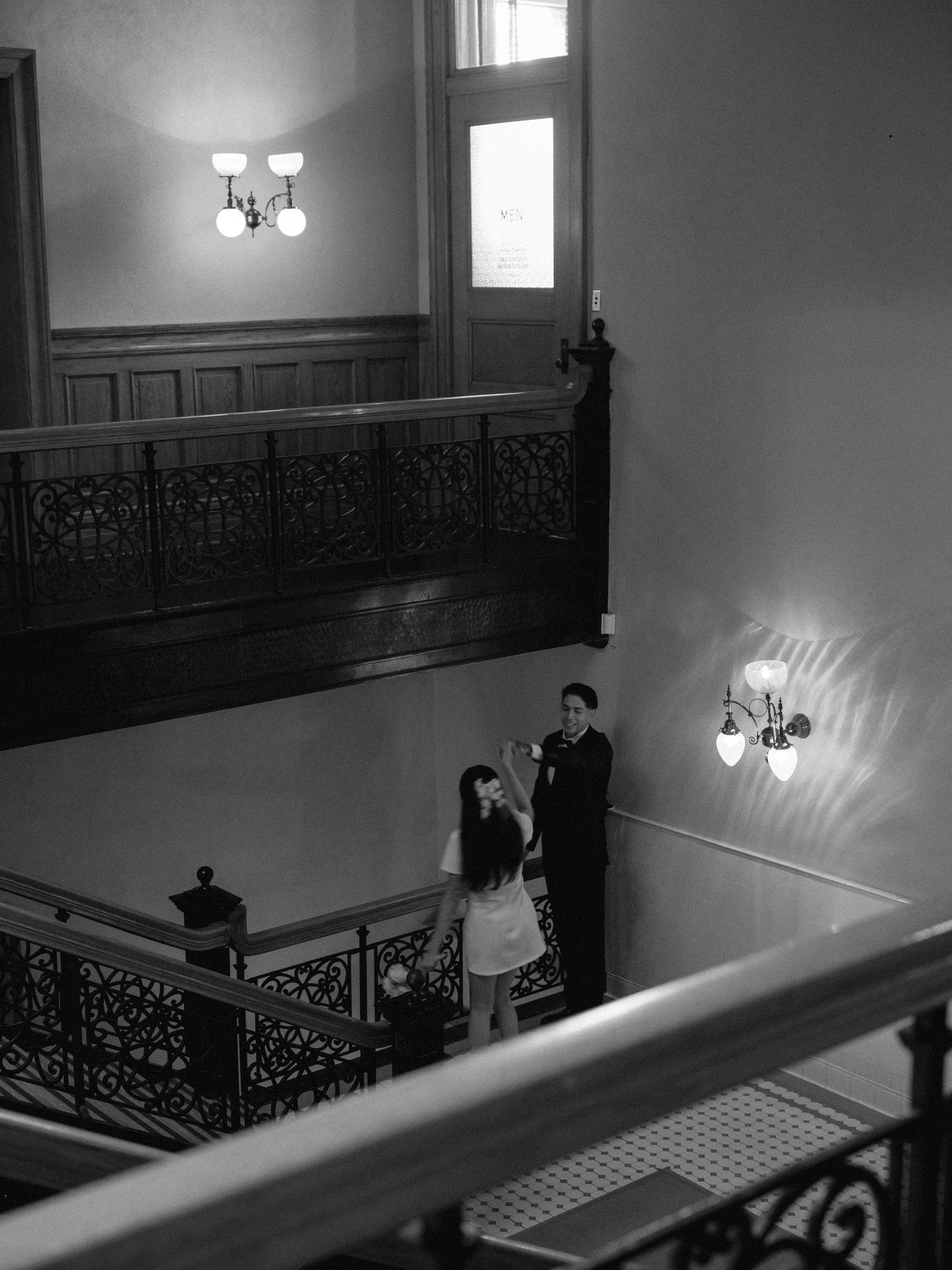 Black and white aerial view of newlyweds on ornate staircase landing in historic building.