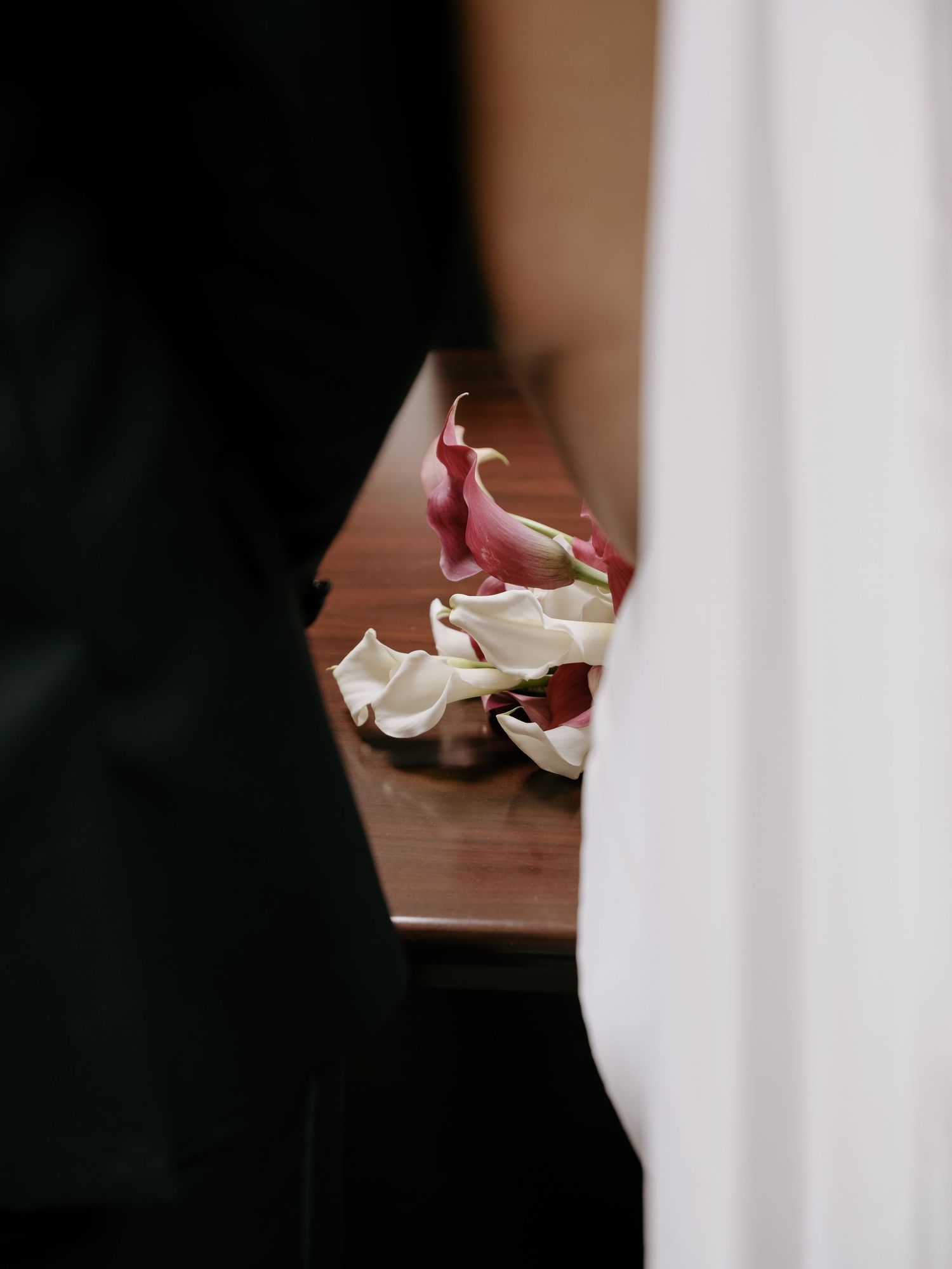 Close-up of pink and white calla lily wedding bouquet resting on a wooden surface during ceremony.