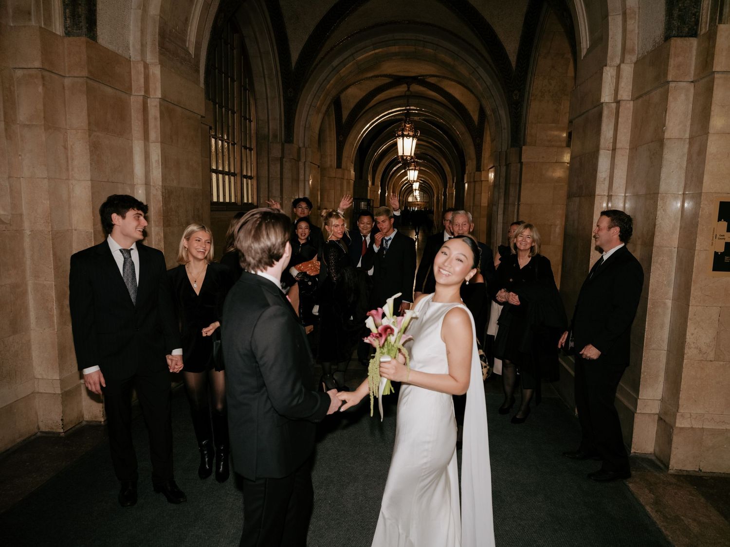 Bride laughing joyfully as groom holds her hands during intimate wedding ceremony in stone hallway.