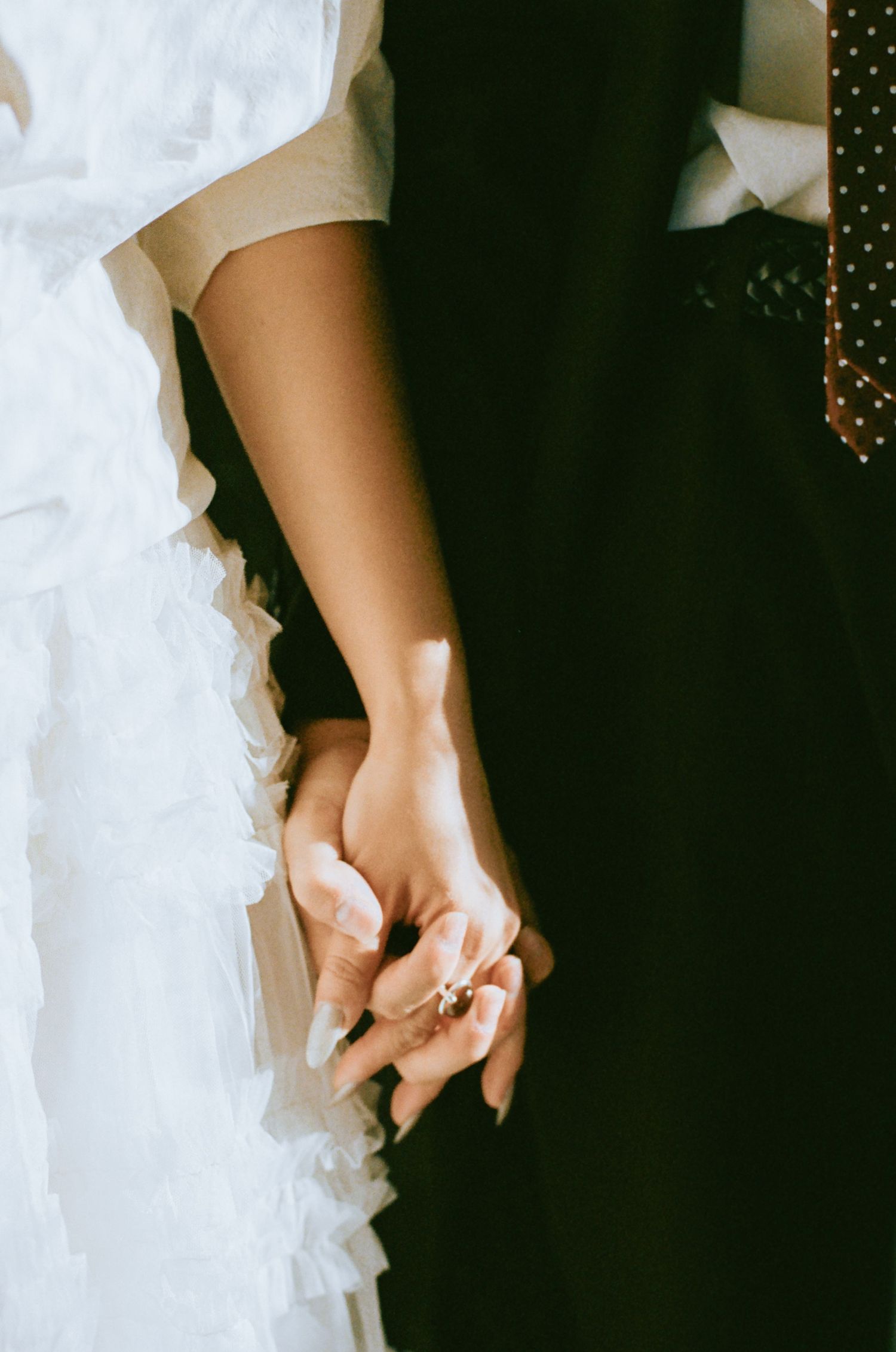 Close-up of bride and groom holding hands, bride wearing a delicate ring and white ruffled dress.