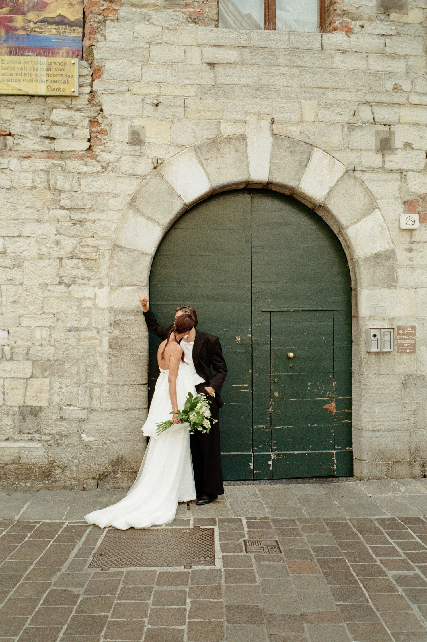 Bride and groom sharing a romantic kiss in front of a rustic green arched door in Italy.