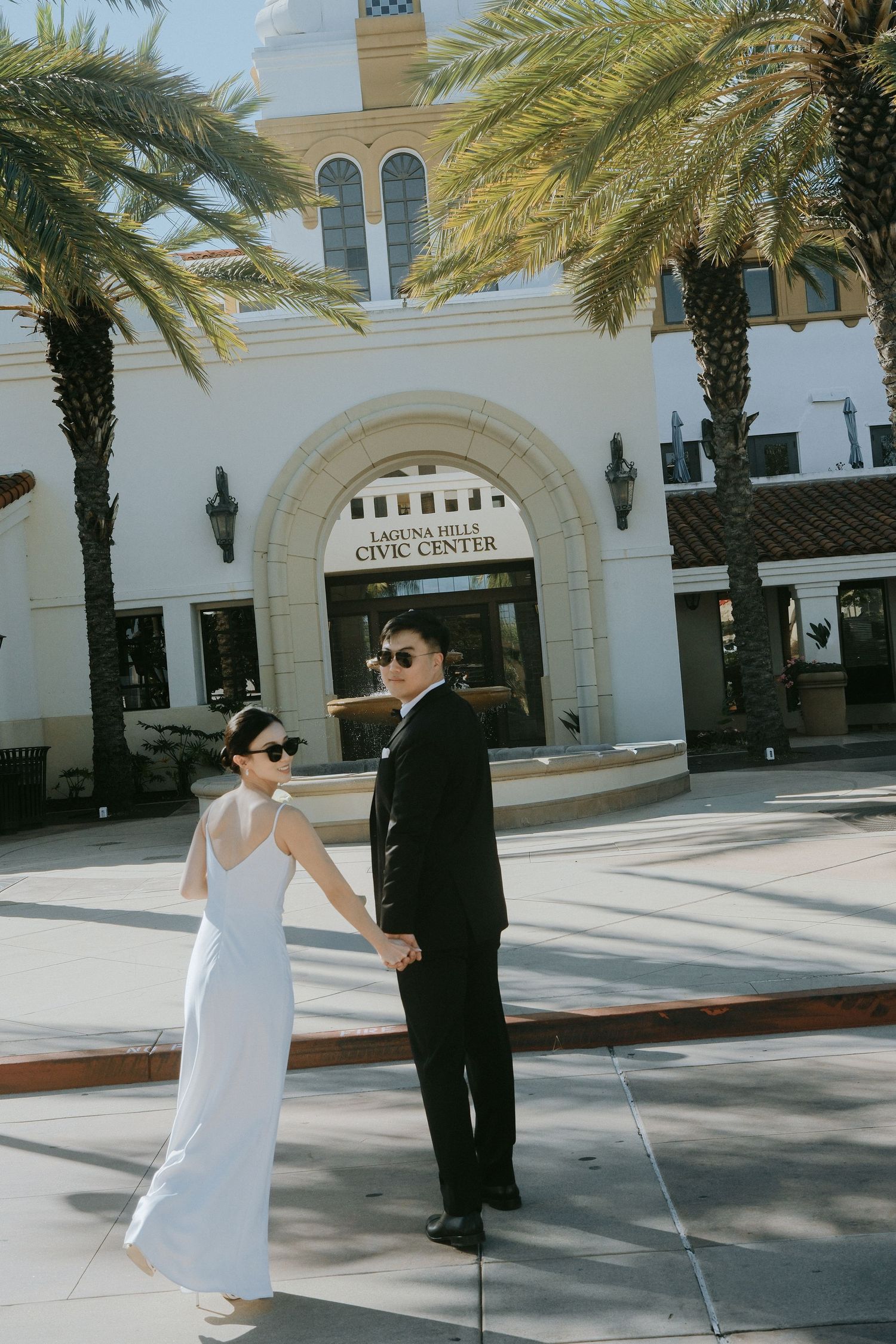 Bride in white dress and groom in black suit holding hands at Laguna Hills Civic Center.