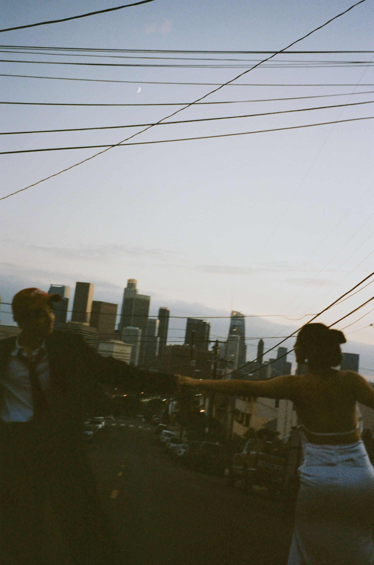 Two people standing apart on urban rooftop at dusk, reaching toward each other with city skyline backdrop.