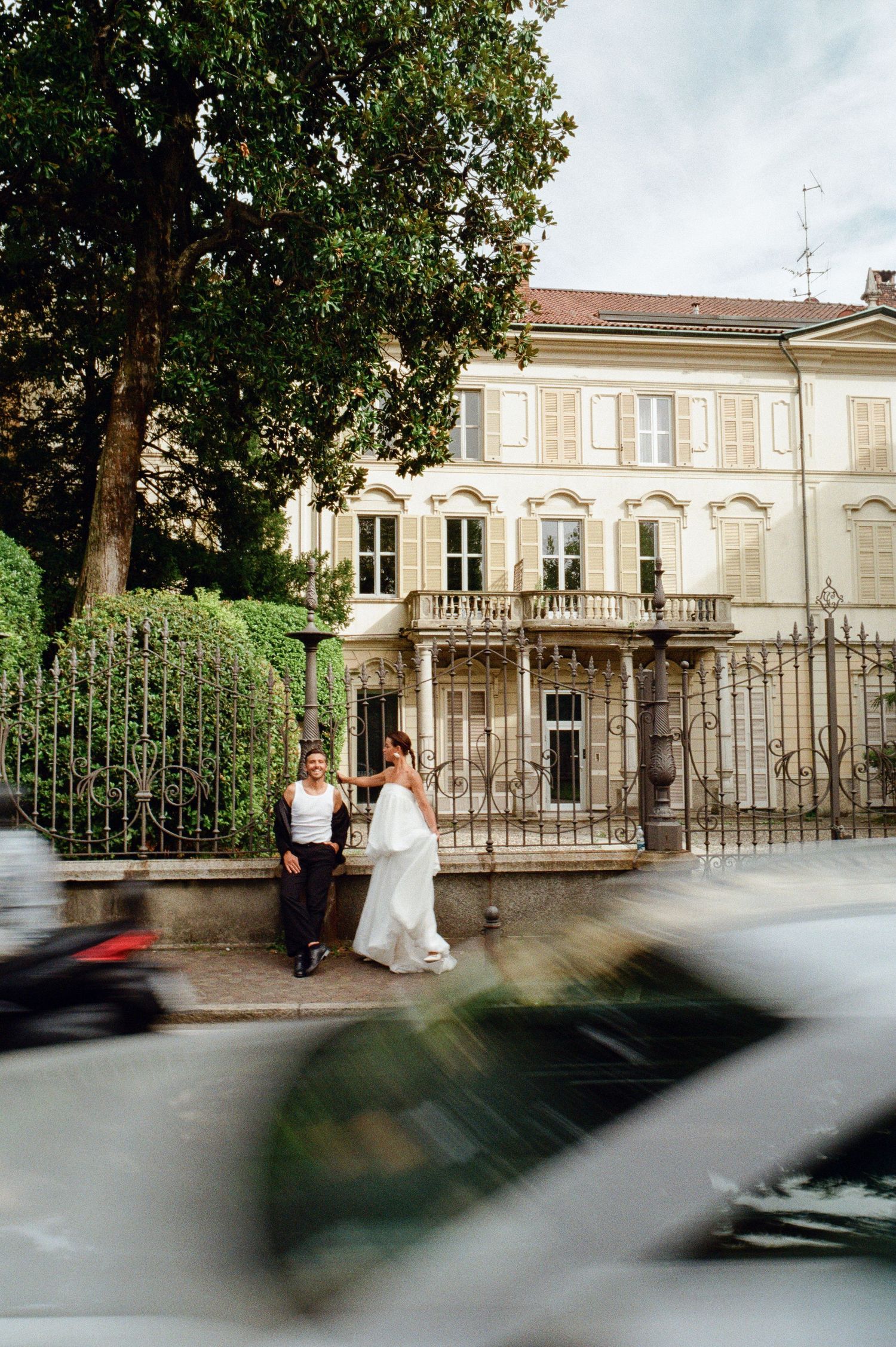 Bride in white gown and groom in white tank top pose before elegant Italian villa.