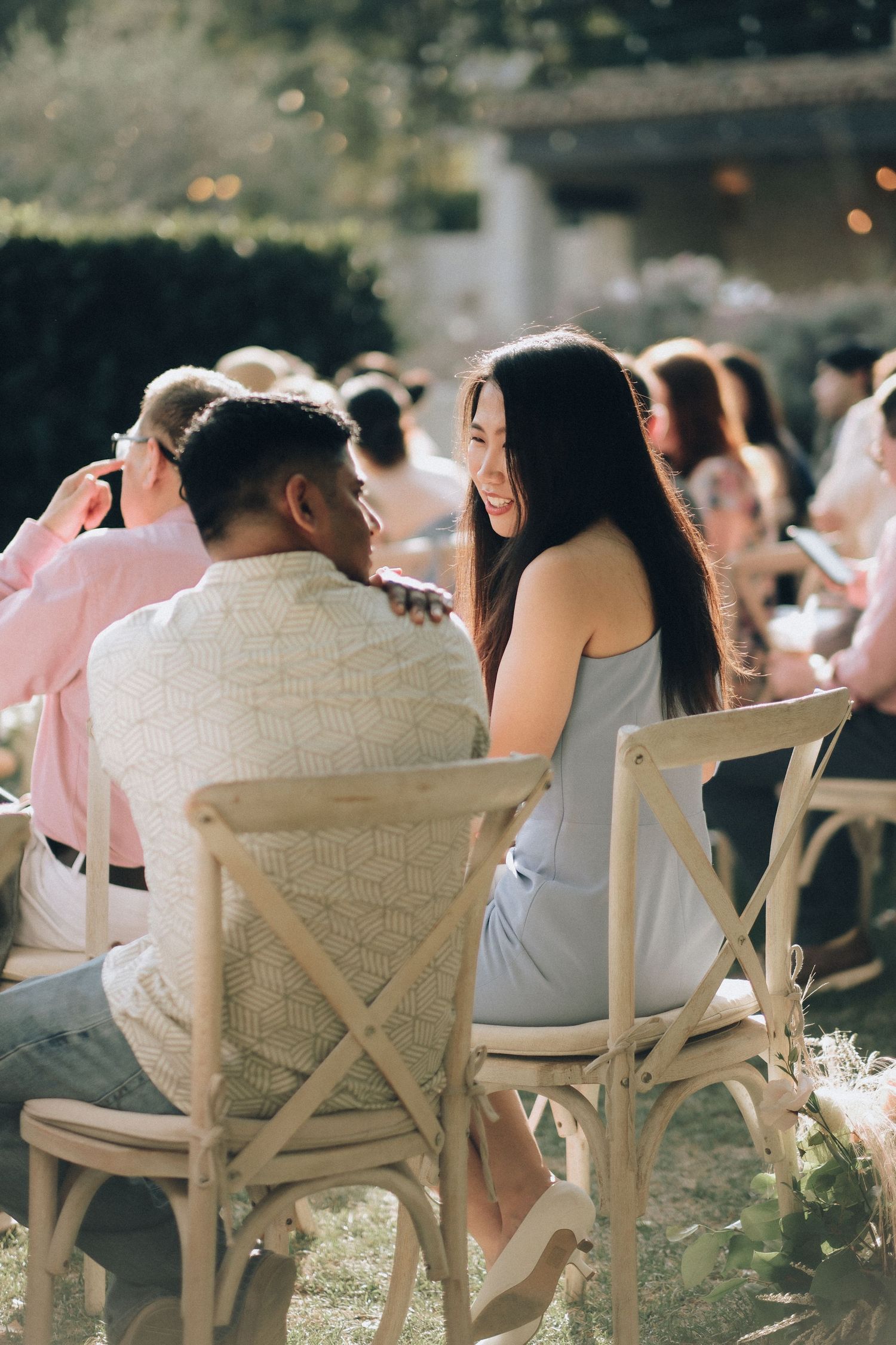 Smiling couple sharing a tender moment seated together at a sunny outdoor wedding ceremony in a garden.