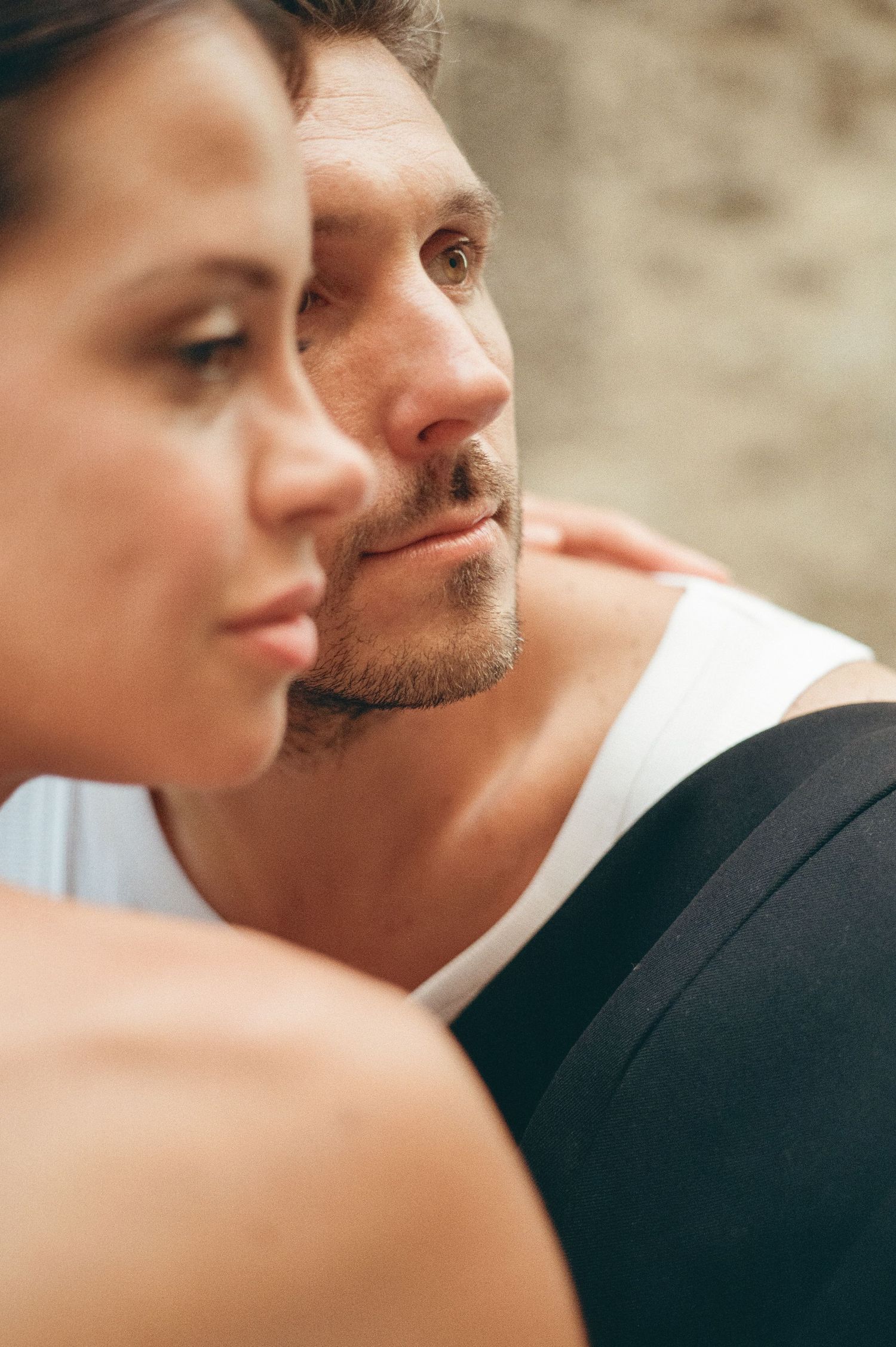 Close-up portrait of a groom in a white tank top gazing thoughtfully beside his bride in Italy.