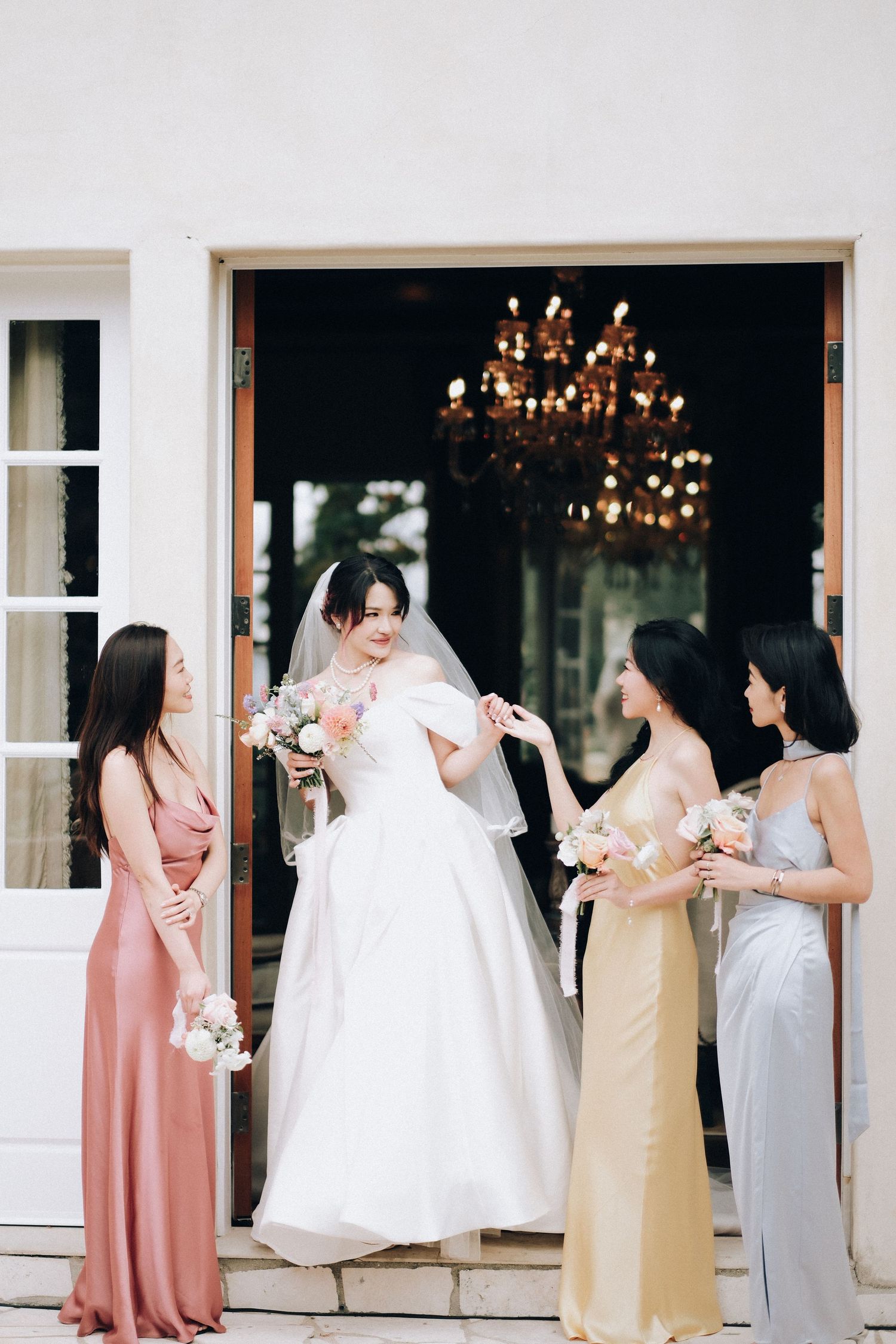 Bride in white ball gown stands with three bridesmaids in colorful satin dresses at venue entrance.