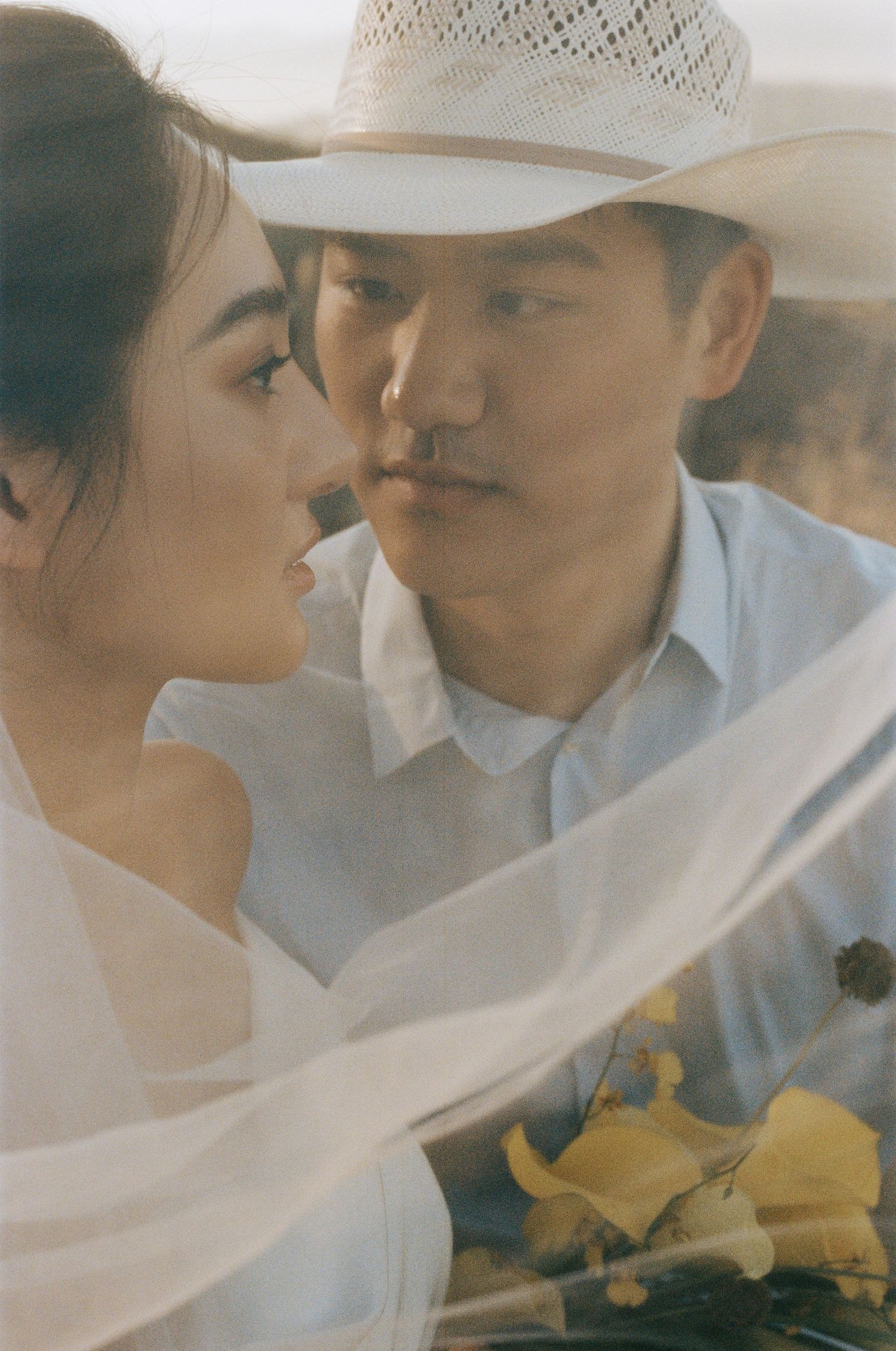 Intimate close-up of bride and groom nearly kissing, framed by a flowing white veil.