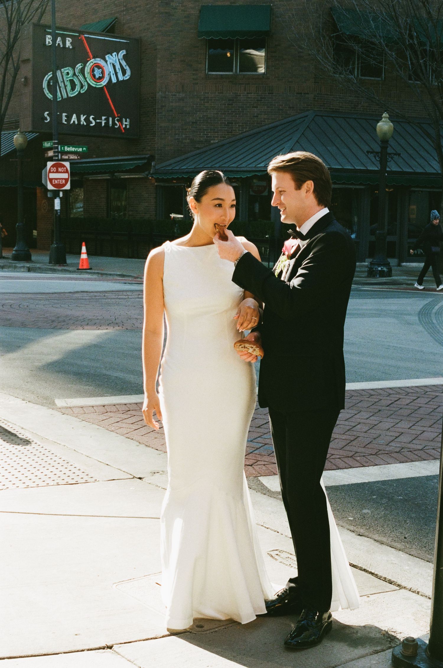 Elegant bride in a sleek white gown and groom in black tuxedo pose outside Gibsons Bar Steaks Fish in Chicago.
