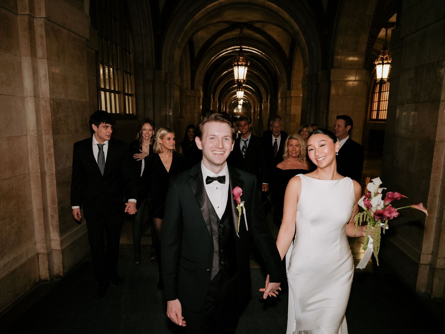 Newlyweds leading wedding guests through dramatic gothic arched corridor after ceremony.